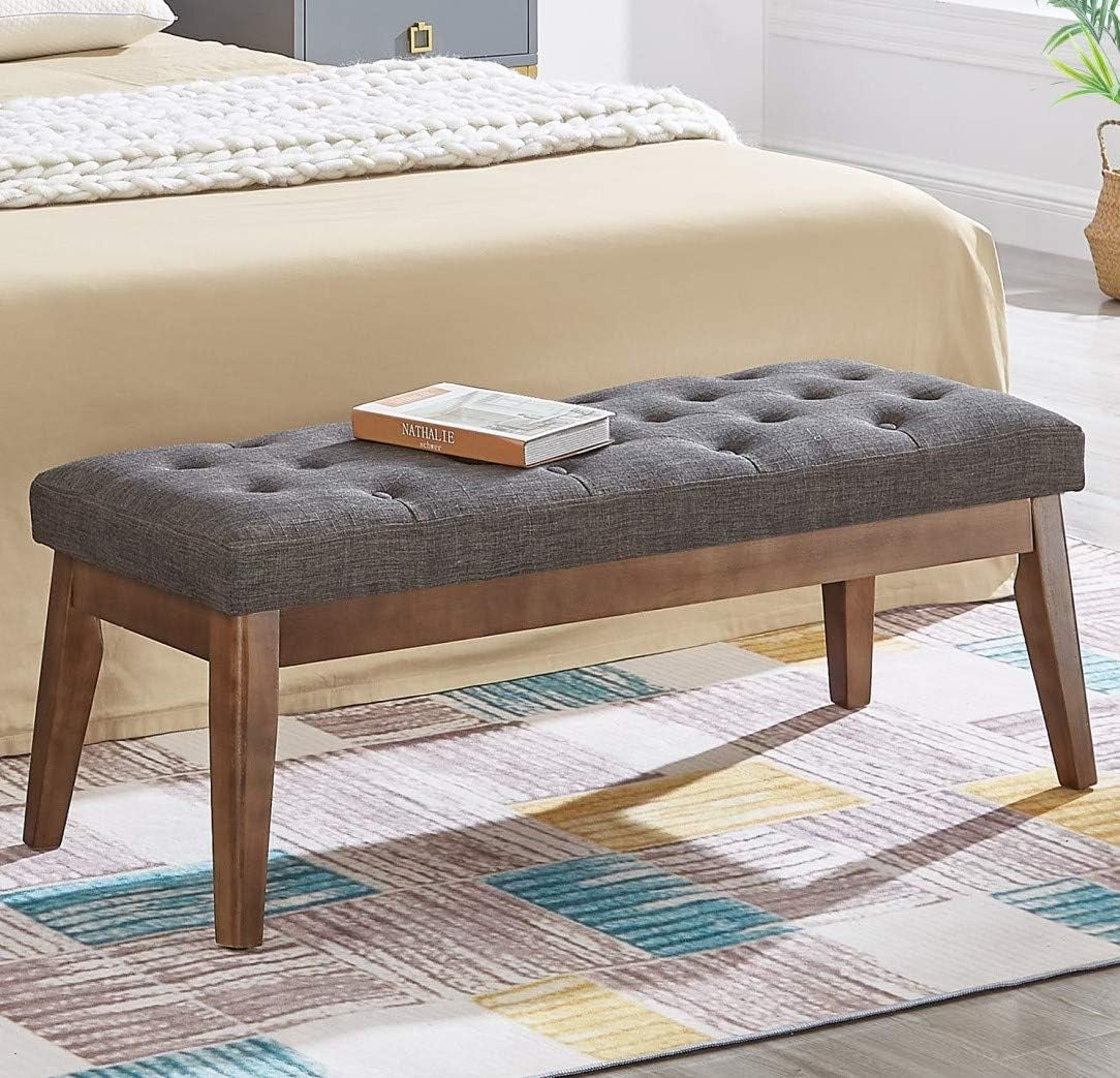 Dark gray button-tufted bench with wooden legs and a book on top at the foot of a bed