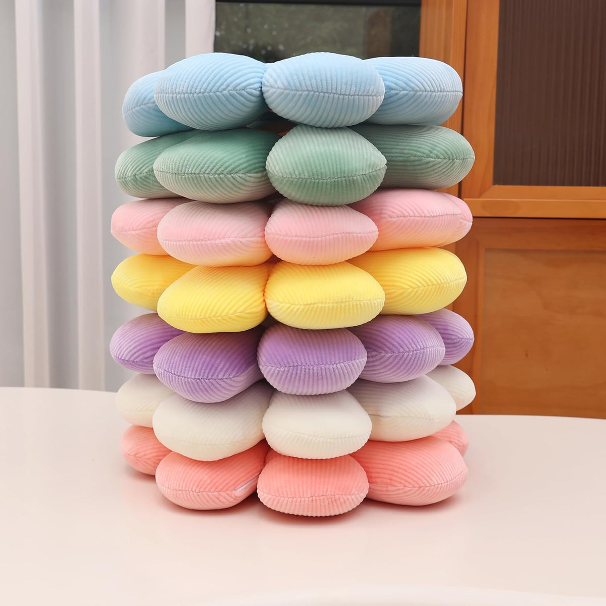 Stacked assortment of daisy throw pillows in purple, yellow, pink, green and blue shown from the side