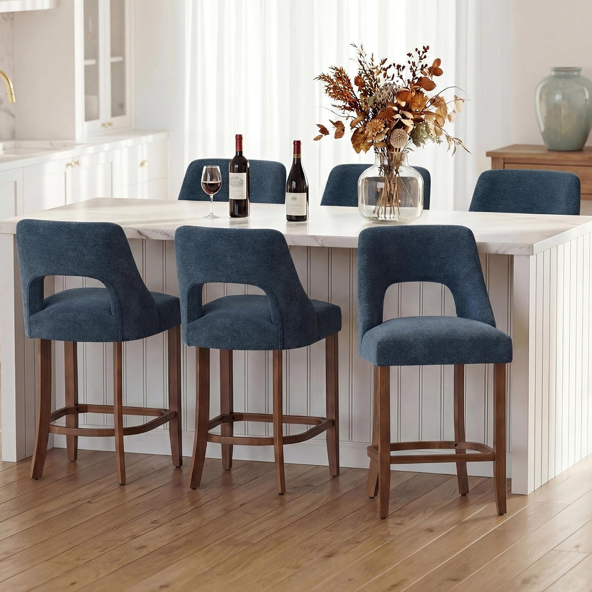 Three blue upholstered counter stools placed at a white kitchen island with decorative vase and wine.