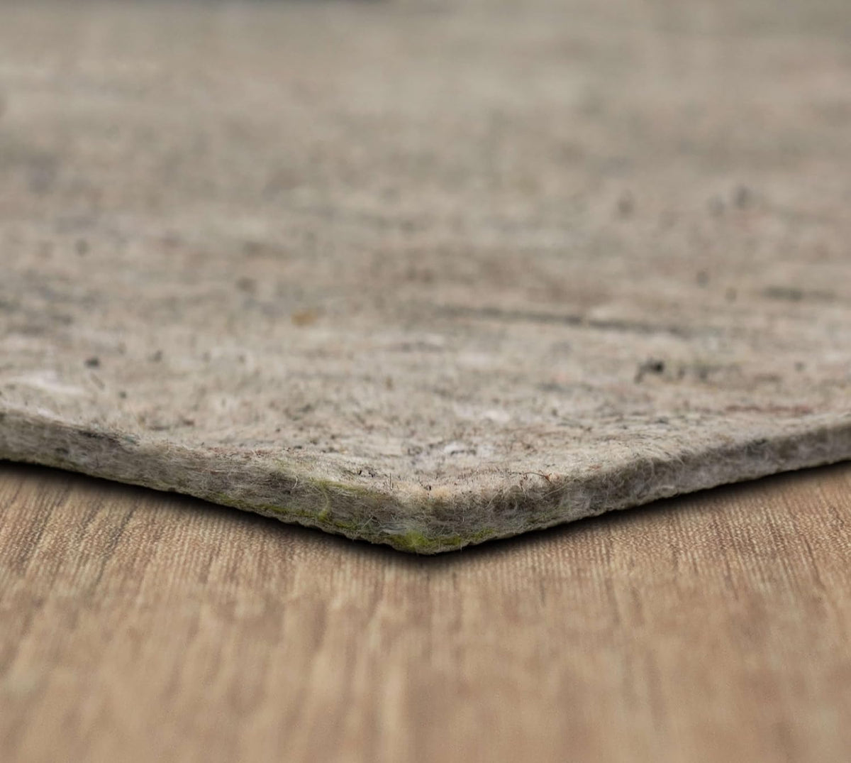 Low-angle close-up of a pad corner on wood, showing the compressed felt edge and small colored fiber flecks.