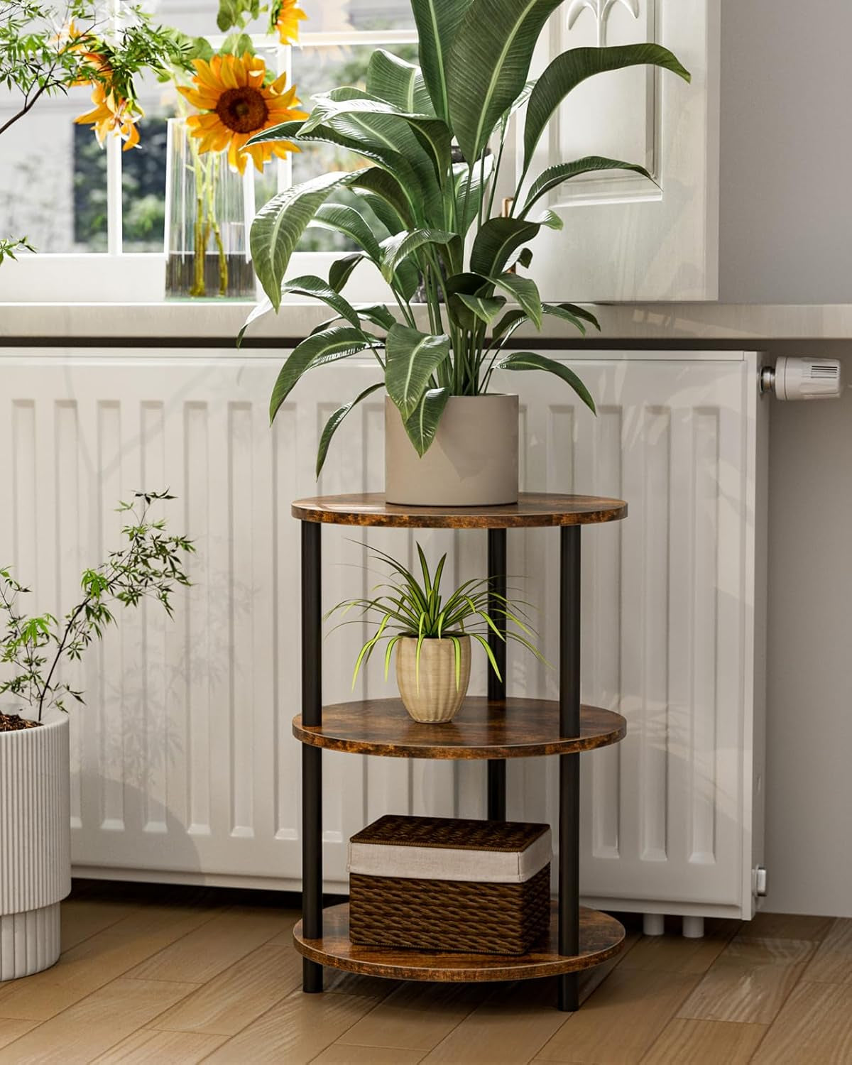 Three-tier round table holding potted plants in front of a bright window radiator.