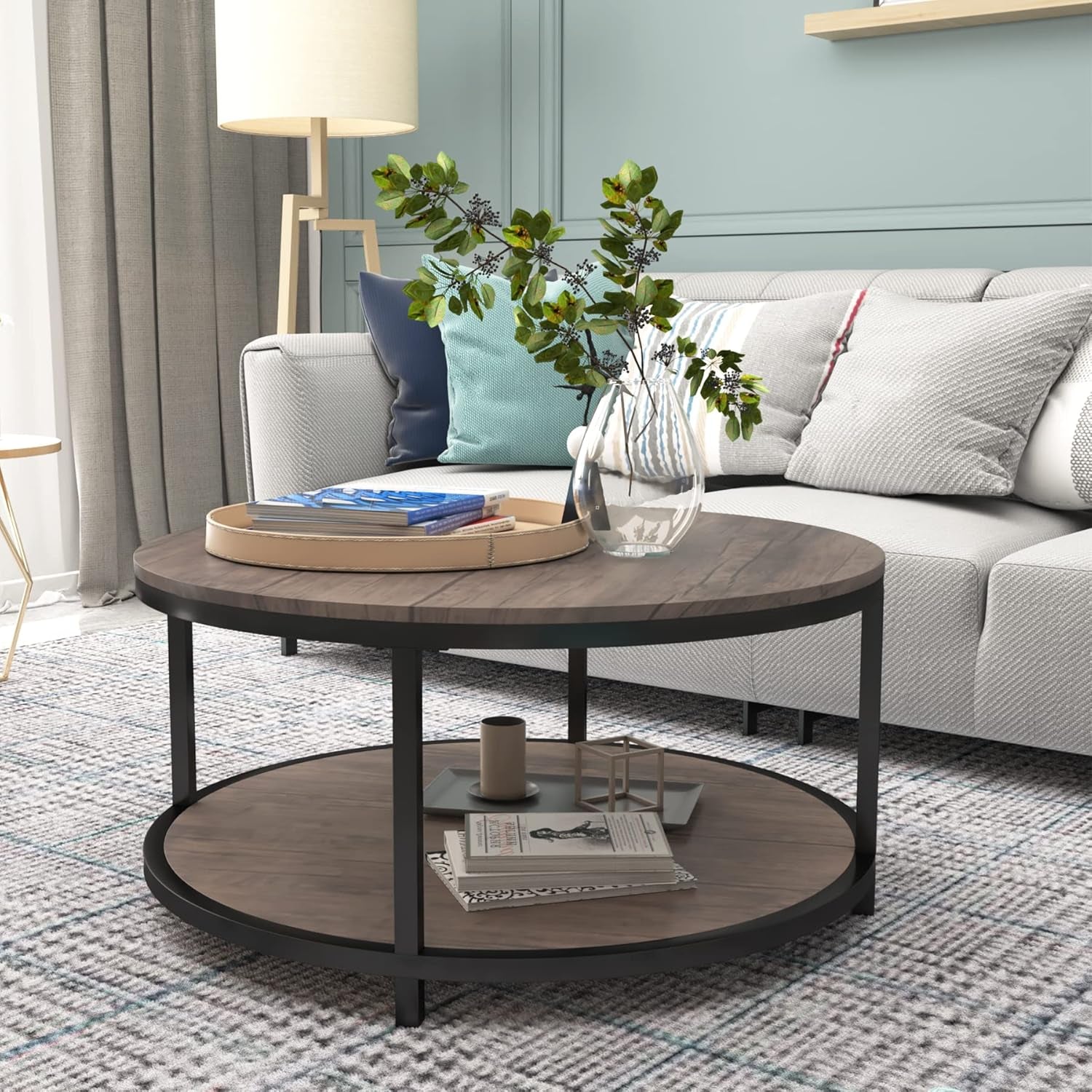 Round two-tier coffee table with vase and books in front of a light gray sofa