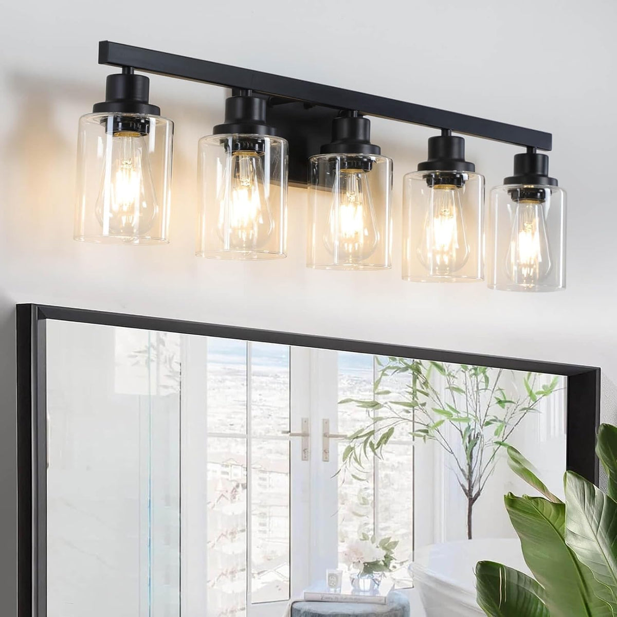 Five-light matte black vanity fixture with clear cylindrical shades glowing above a framed mirror.