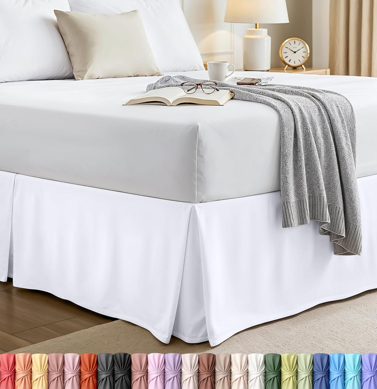 Corner view of a made bed with a white pleated bed skirt and gray throw draped over the mattress