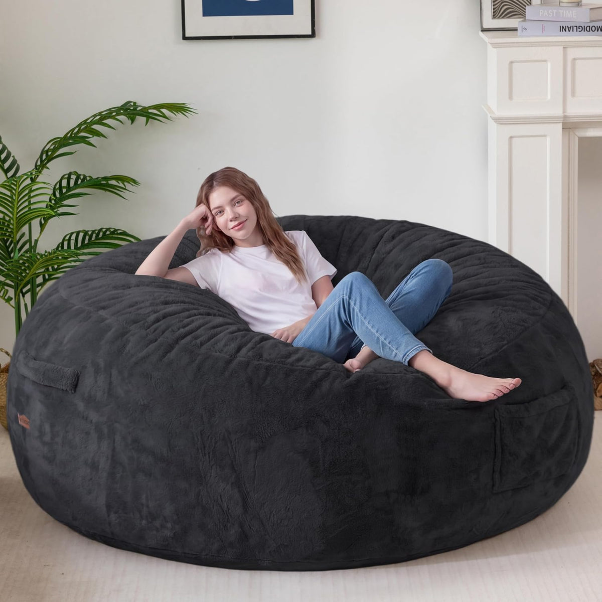 Woman reclining on oversized charcoal faux‑fur bean bag in a bright living room.
