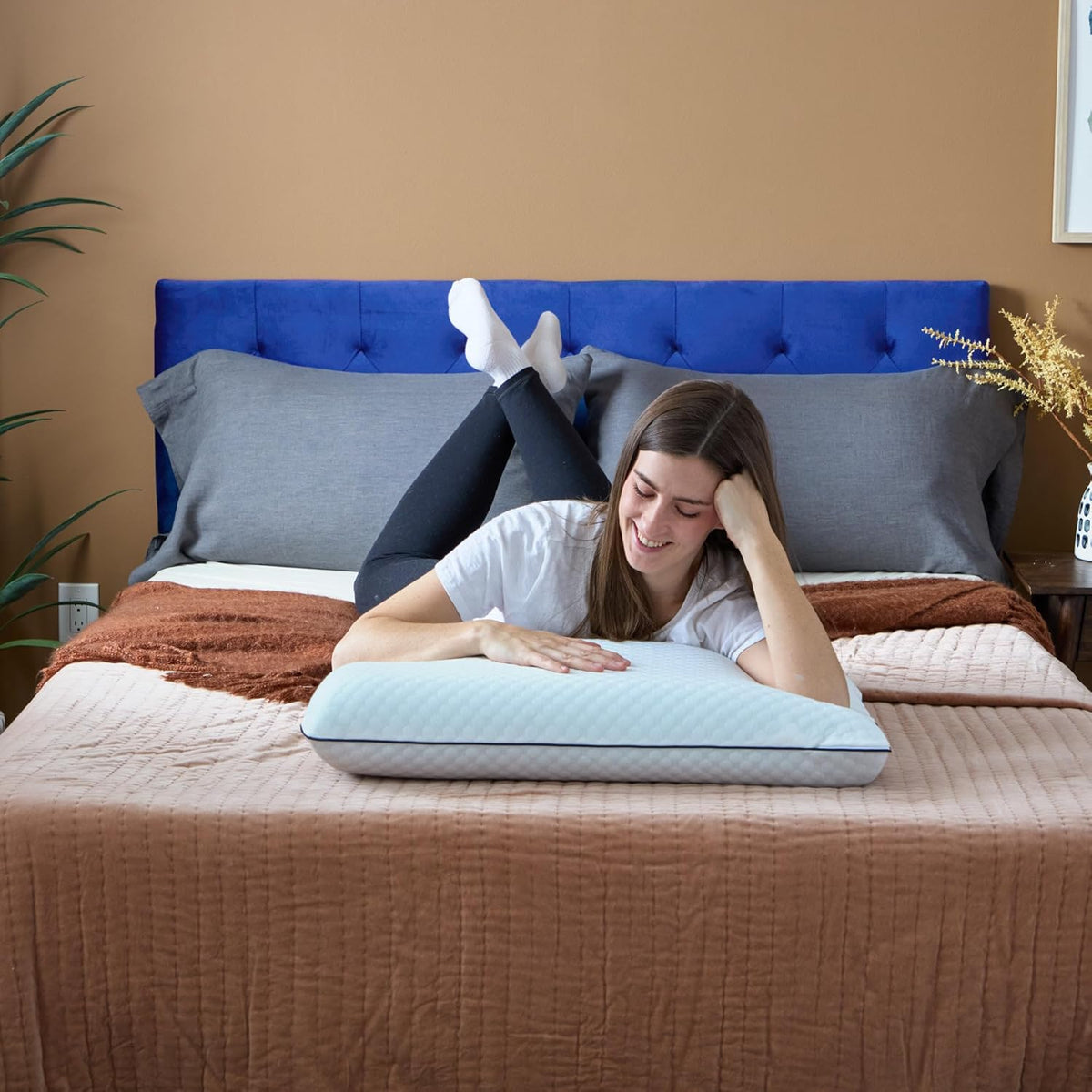 A person resting on a made bed with a hand on the pillow, blue tufted headboard behind