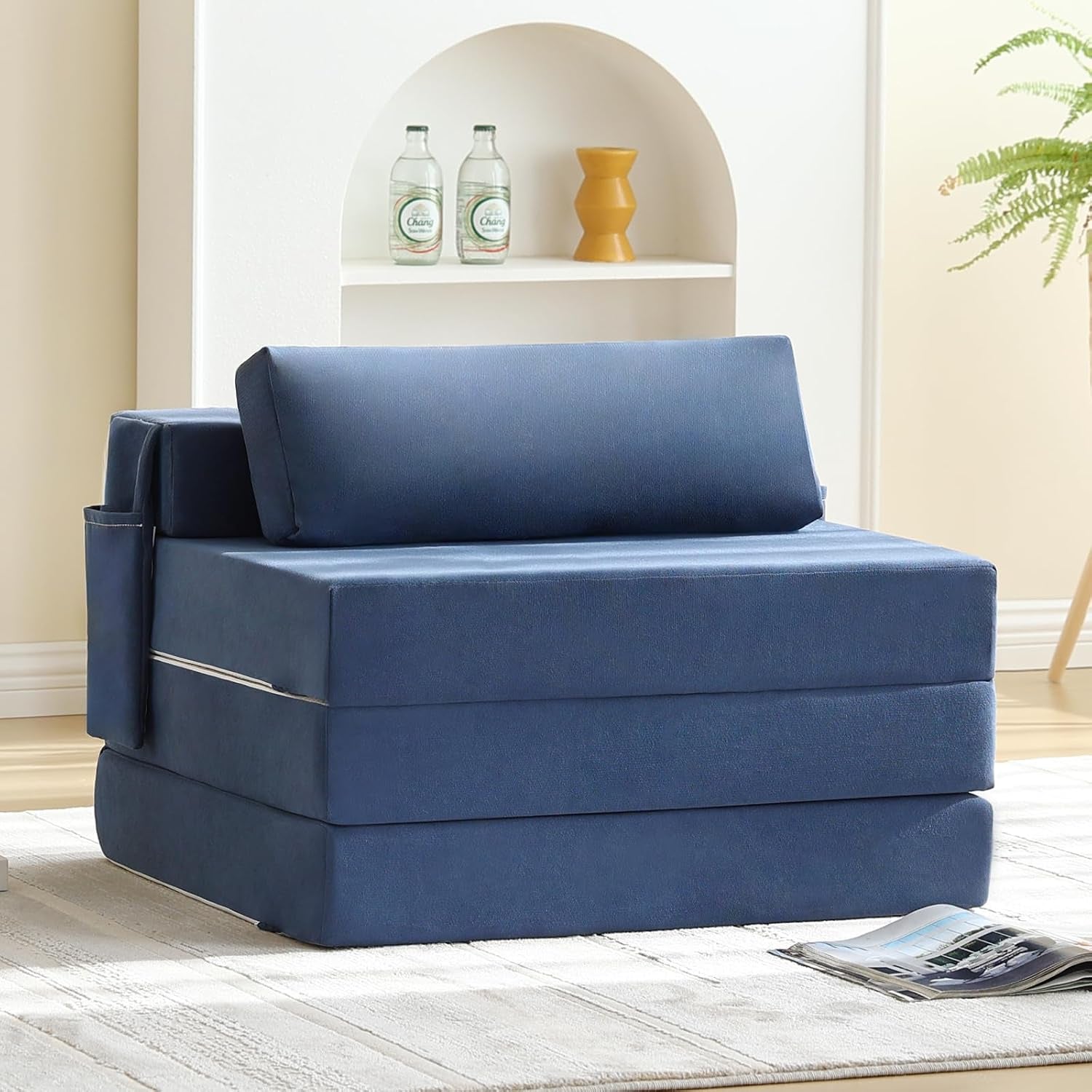 Blue foldable sofa bed chair with side pocket shown in a bright living room setting.