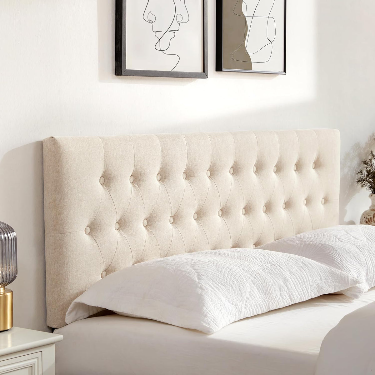Angled close-up of beige linen button tufting and padded edge of the headboard with a pillow in the foreground.