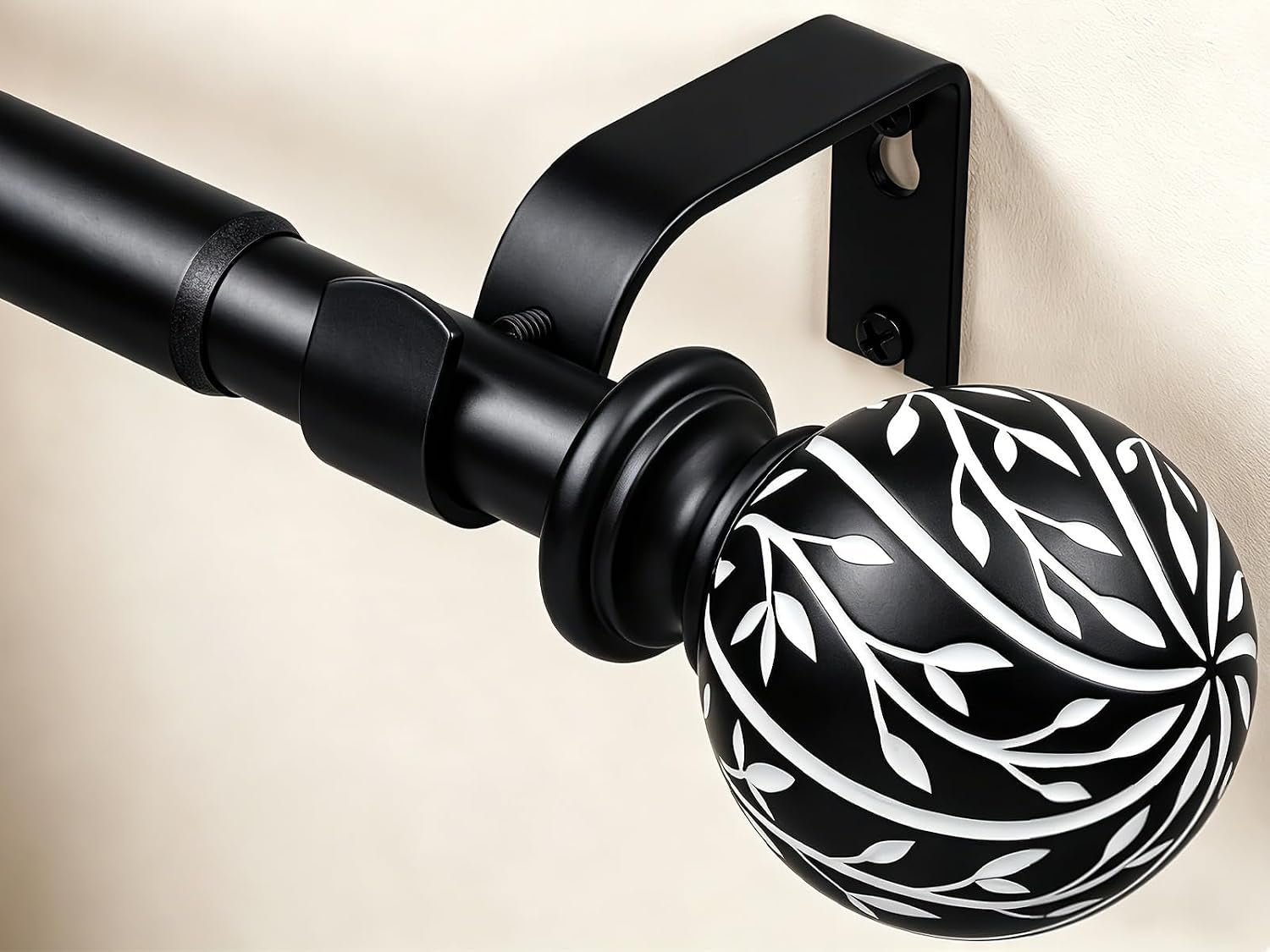 Close-up of matte black rod end with carved spherical finial featuring white leaf pattern and metal bracket