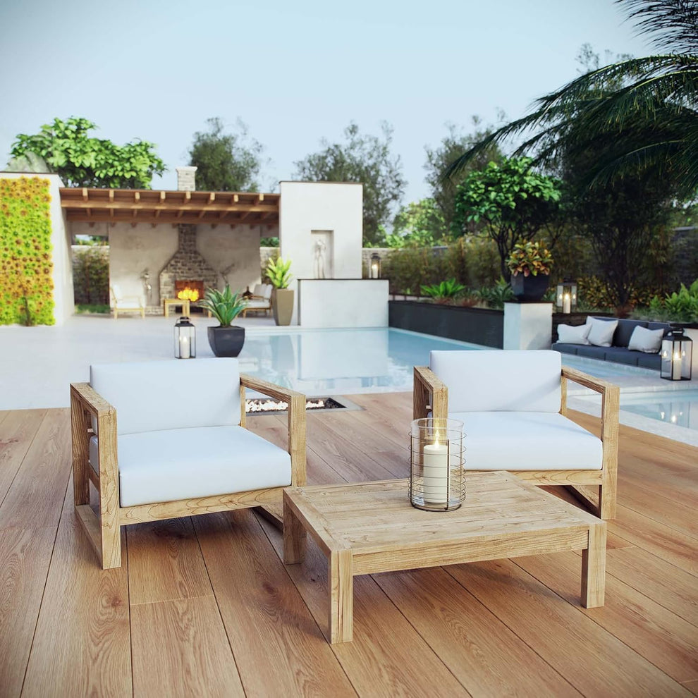 Two teak armchairs flanking a low teak coffee table with candle, pool and lanterns behind