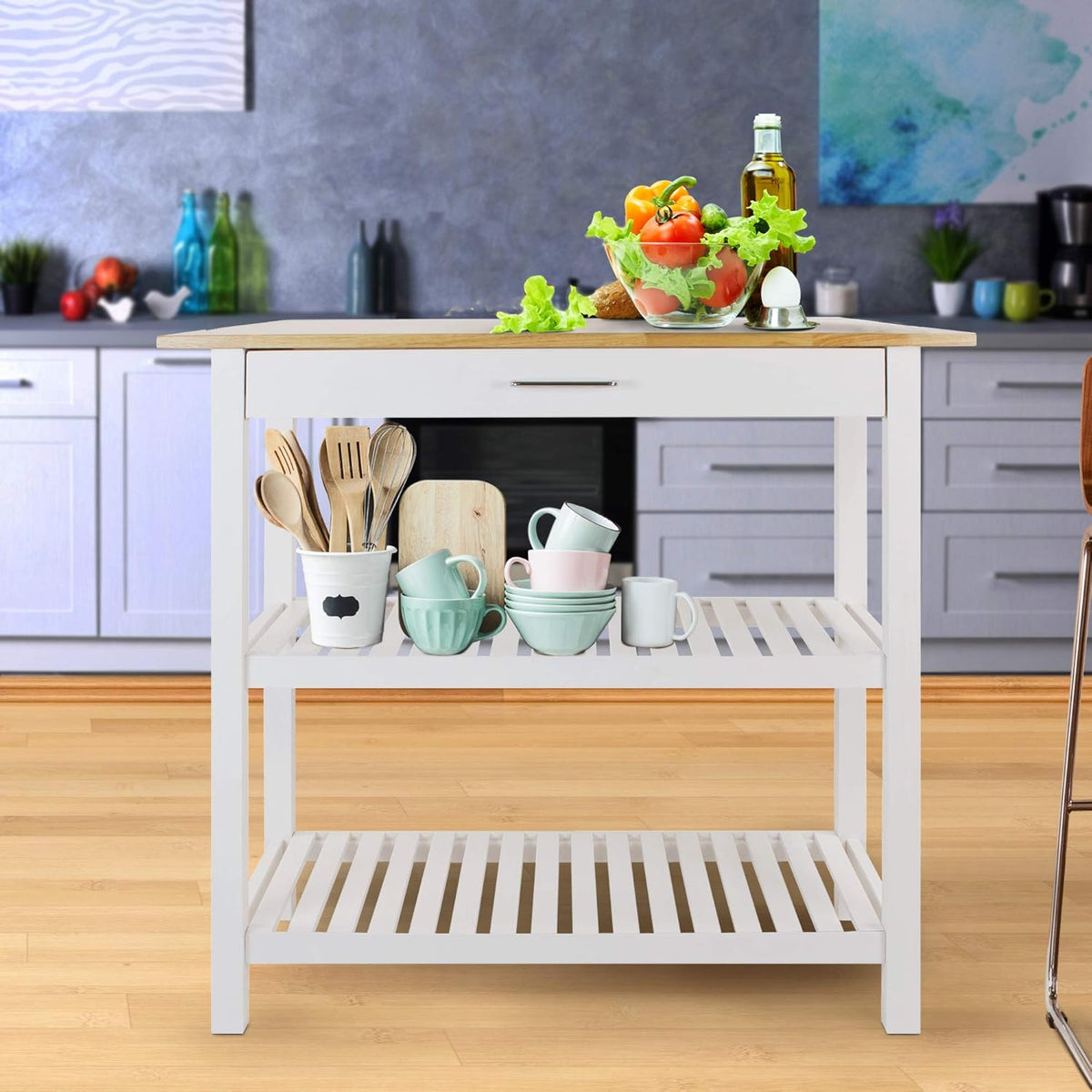 Front view of the island in a staged kitchen with bowls, utensils and produce on the top and middle shelf.