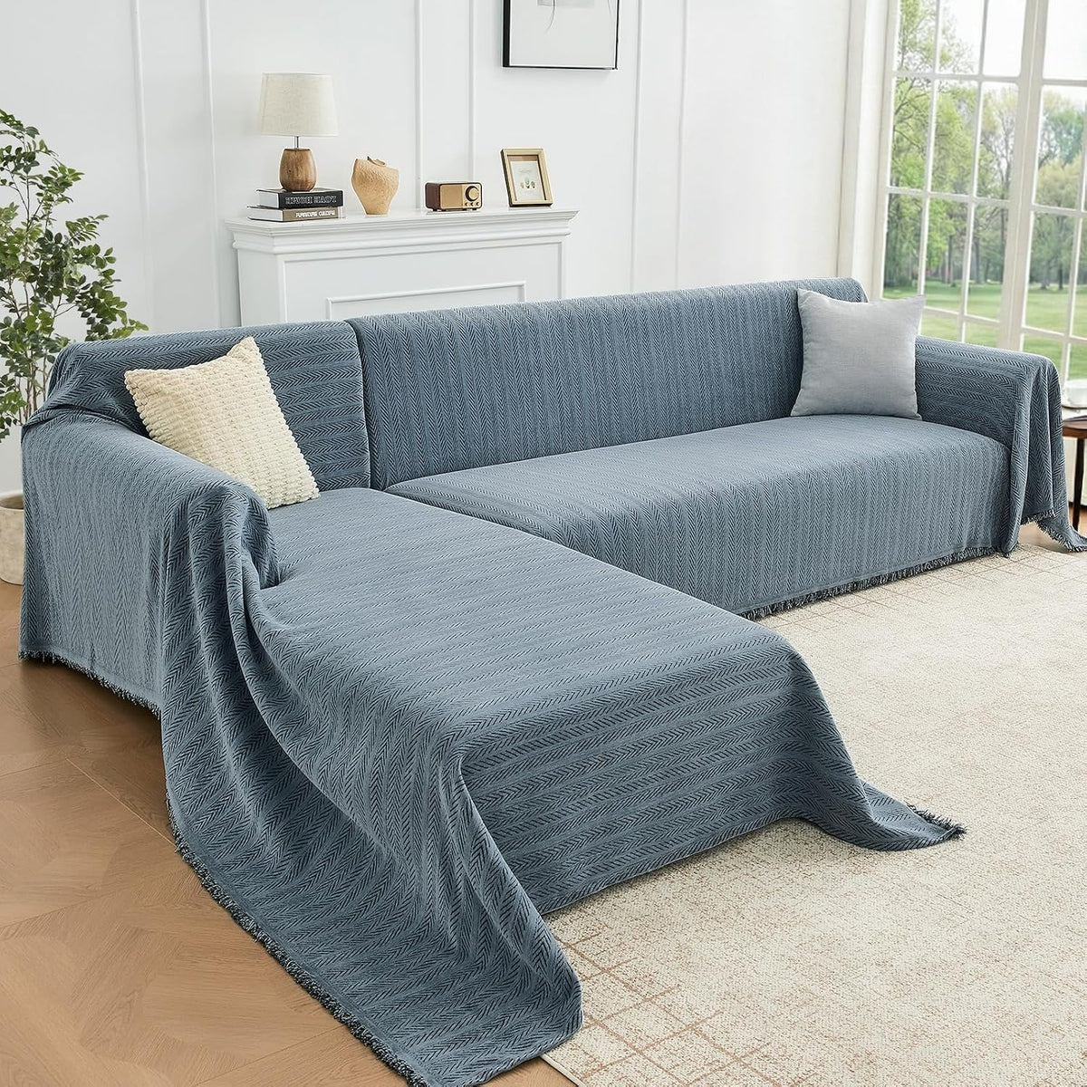 Sectional wrapped in a slate-blue herringbone throw with light grey and cream pillows and a decorative mantel behind.