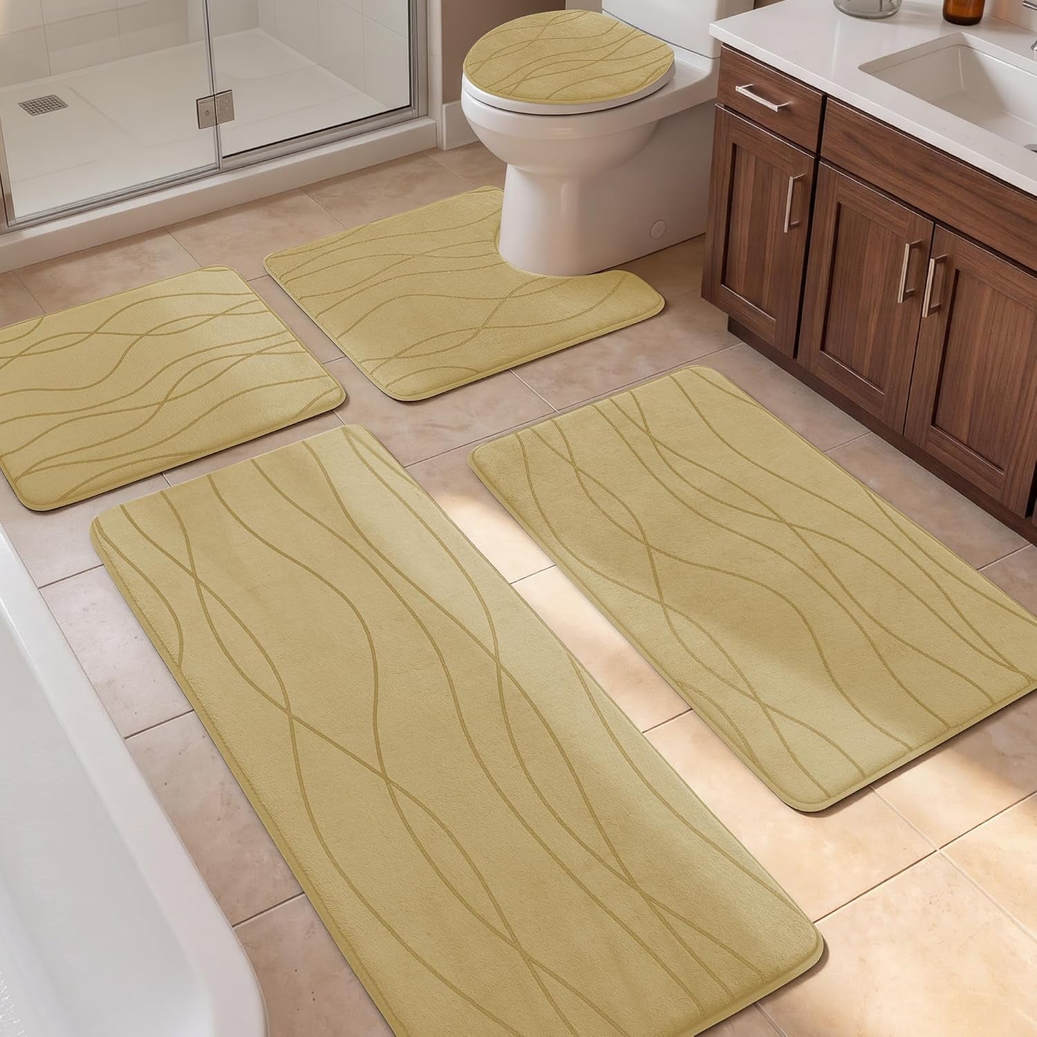 Five-piece beige bath rug set laid out on a tiled bathroom floor near a shower and wood vanity.