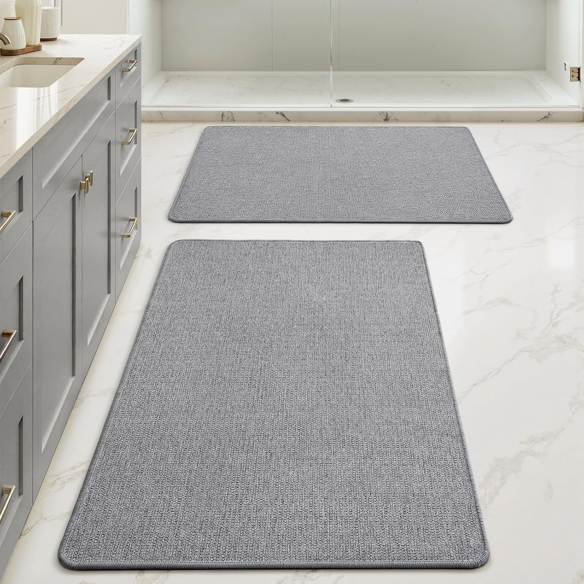 Gray rectangular bath rugs arranged down the floor beside a sink cabinet and shower