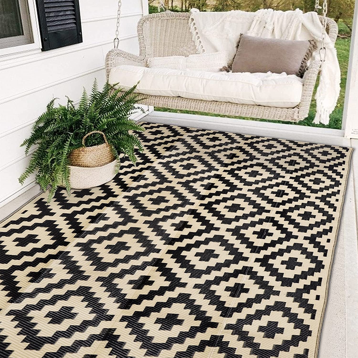 Outdoor porch scene with a black-and-cream geometric rug beneath a woven swing and potted fern.