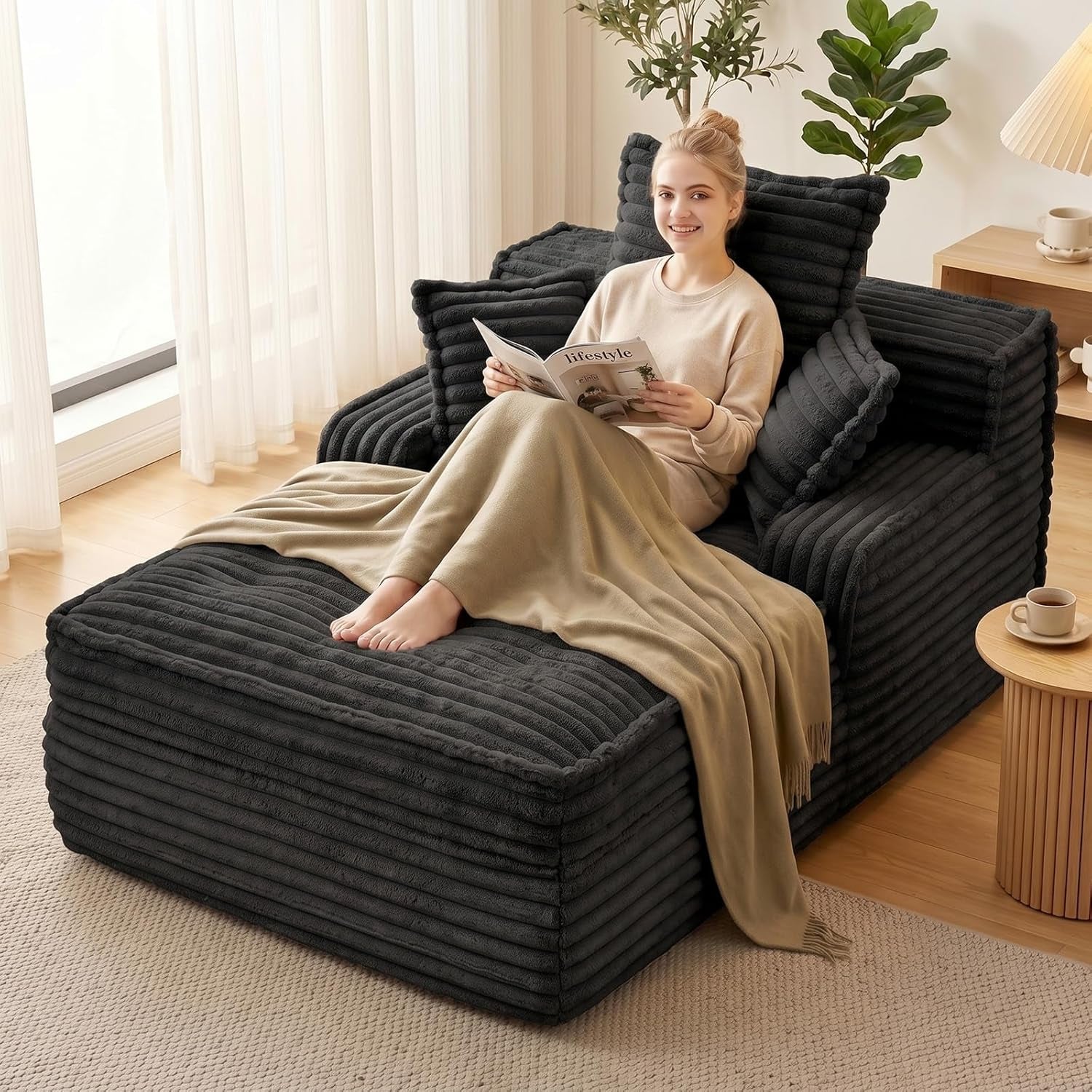Angled view of a black ribbed chaise lounge with a smiling woman reading under a beige throw.