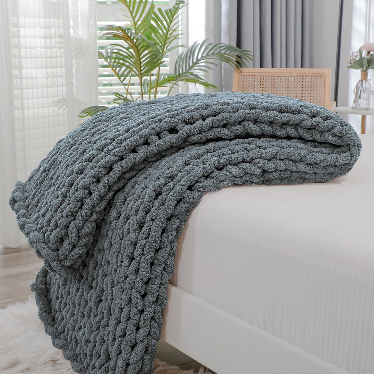Charcoal gray chunky knit blanket folded and layered at the foot of a white bed.