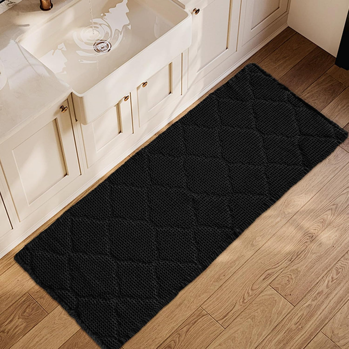 Top-down view of a black waffle-pattern bathroom mat placed along a vanity on wood floor.