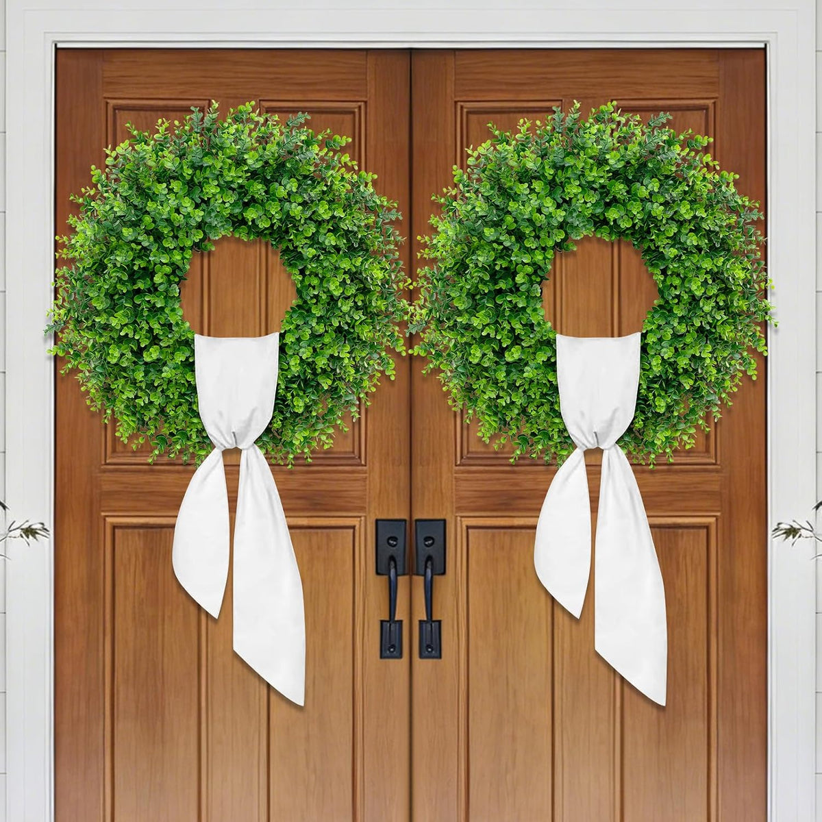 Two identical green boxwood wreaths on double wooden entry doors
