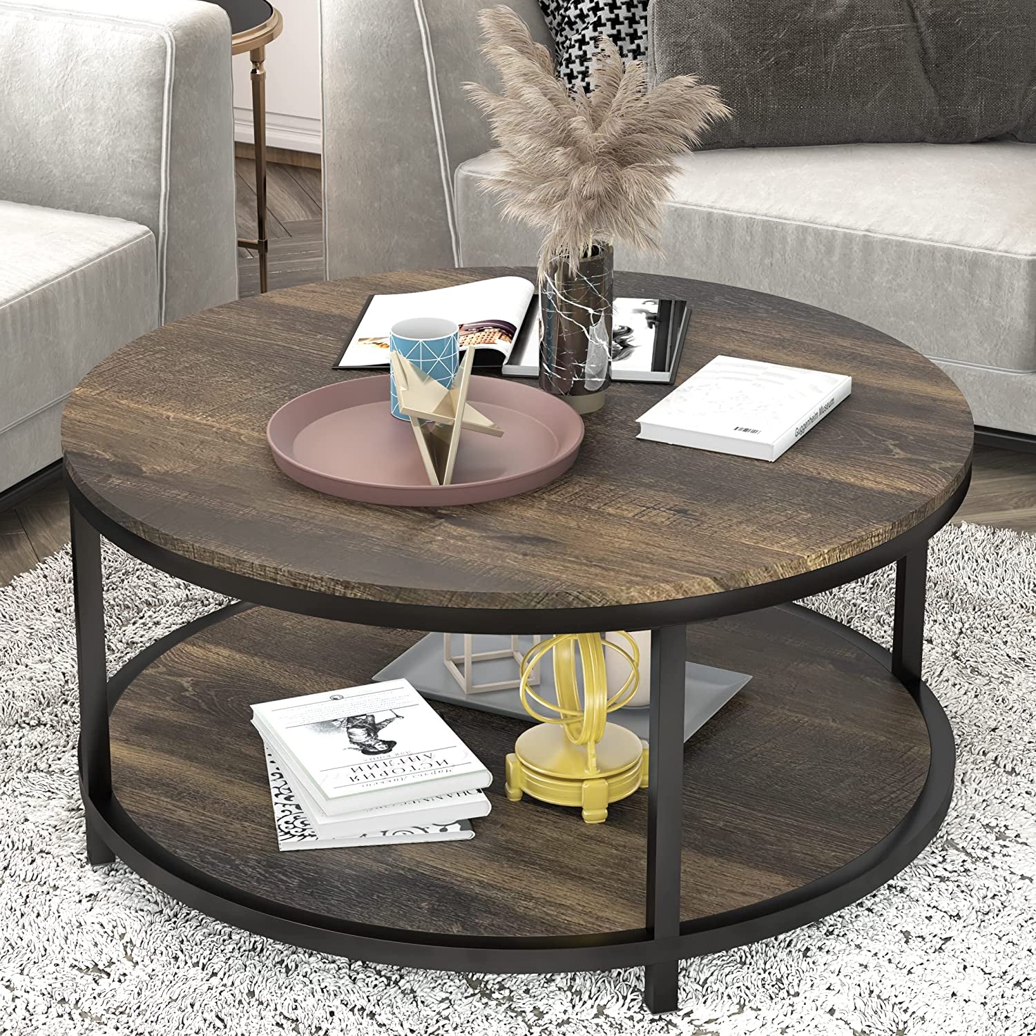 Round two-tier coffee table with a dark wood top and lower shelf, black metal frame, decorative tray and books on top.