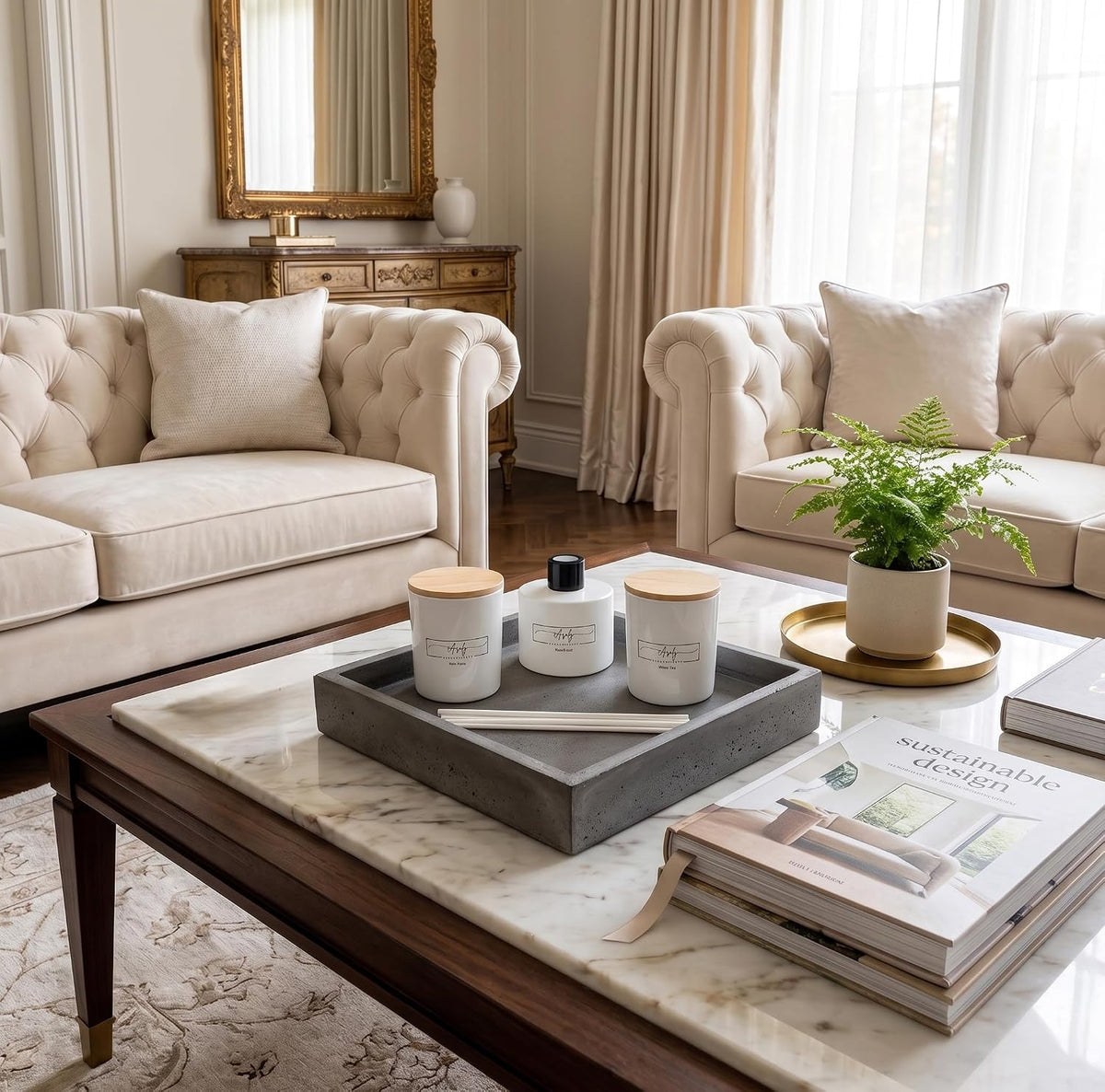 Coffee-table vignette with two lidded white candle jars and a round diffuser bottle on a gray tray, a fern and stacked books