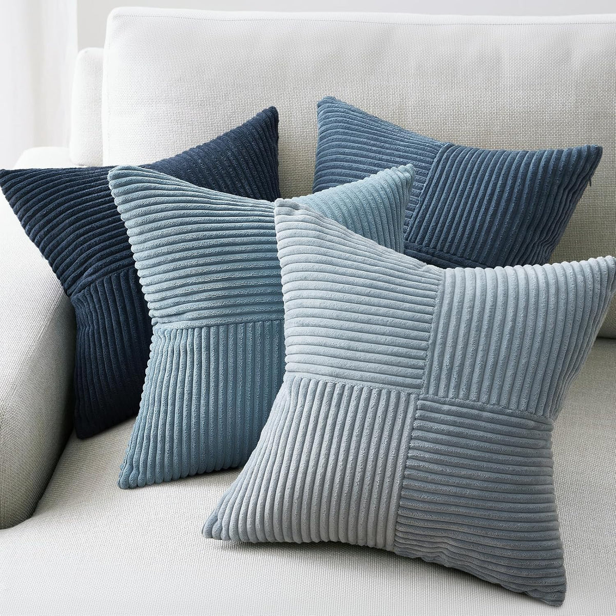 Four ribbed velvet pillow covers in blue-gray tones arranged on a light fabric sofa.