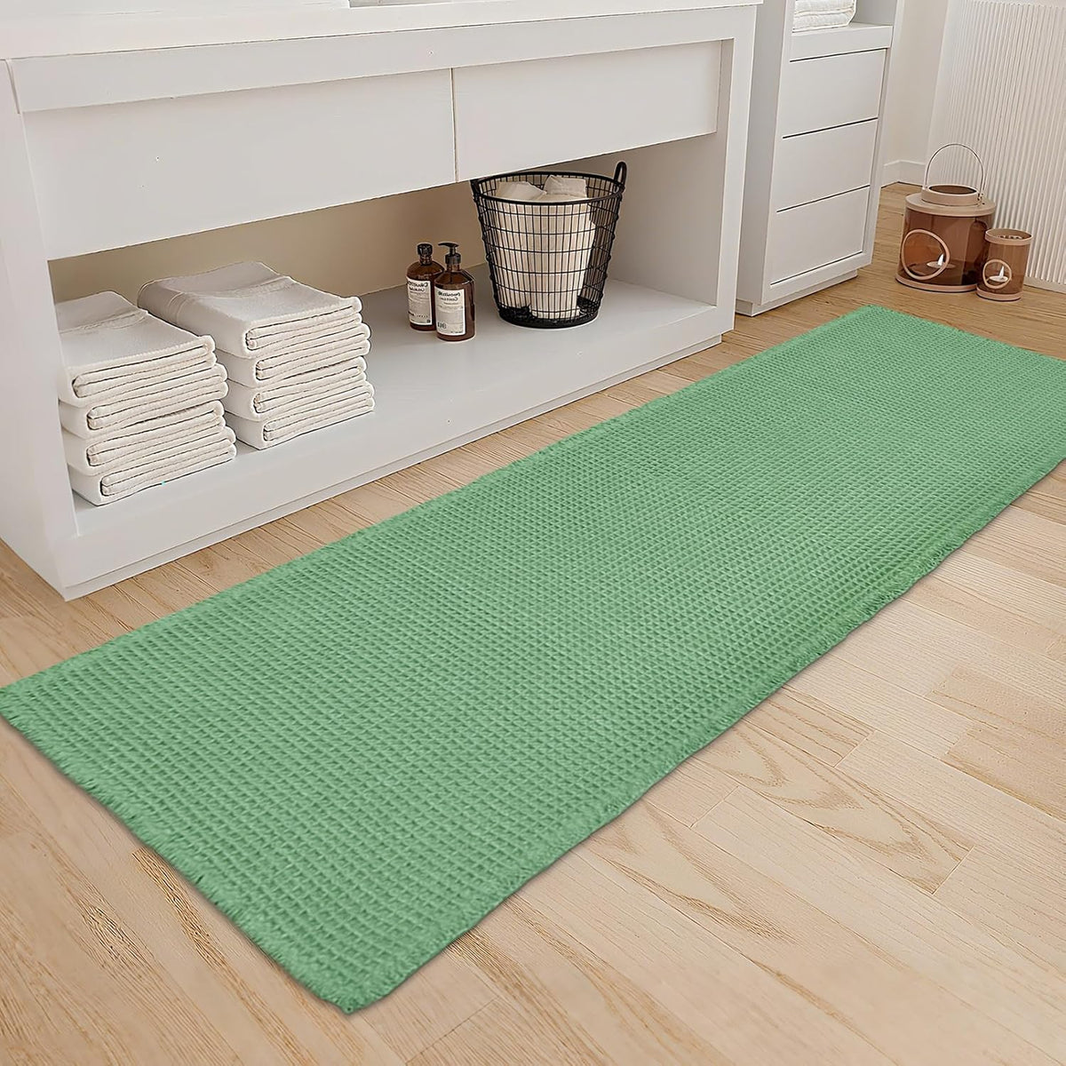 Green waffle-texture bath runner laid along a wooden floor beside a white vanity
