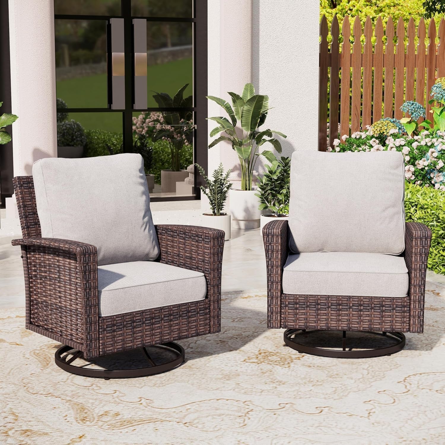 Pair of brown wicker swivel chairs with light beige cushions on a patio rug near potted plants.