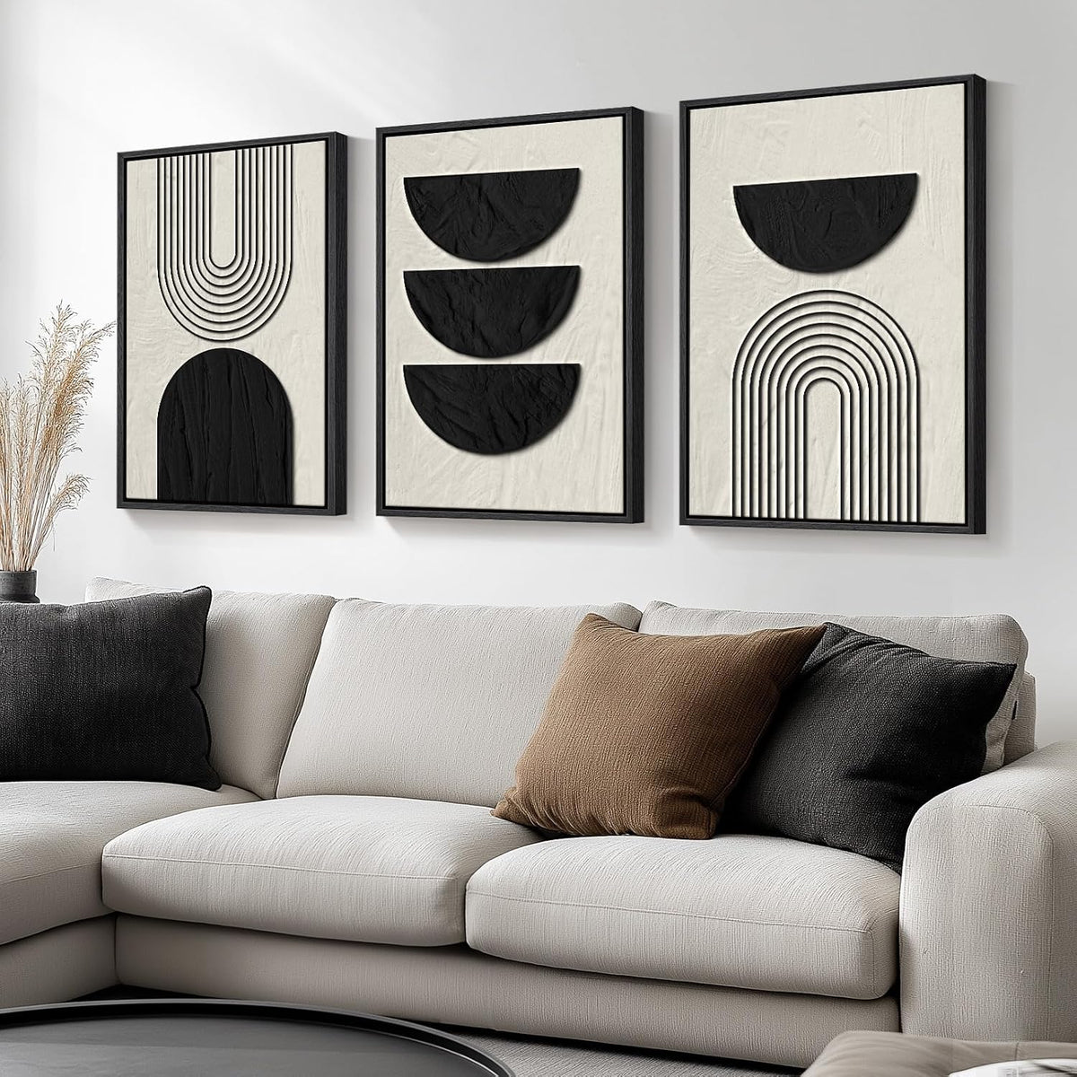 Three framed panels showing stacked semicircles and arch lines in black on textured beige above a sofa with pillows.