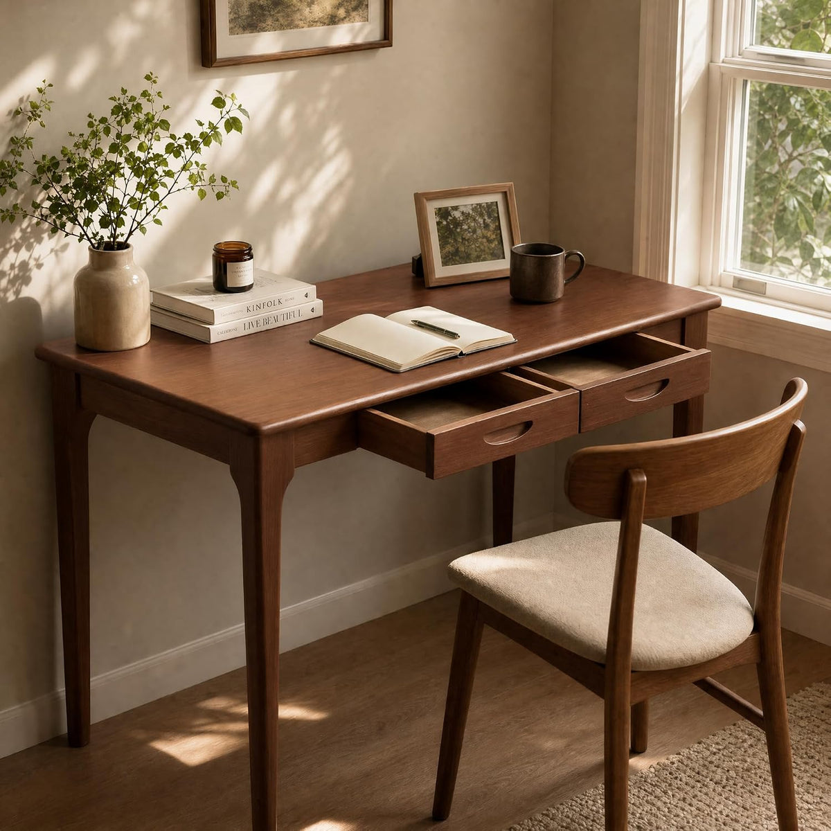 Desk shown near a window with a small vase of greenery, two drawers partially open and a wooden chair.