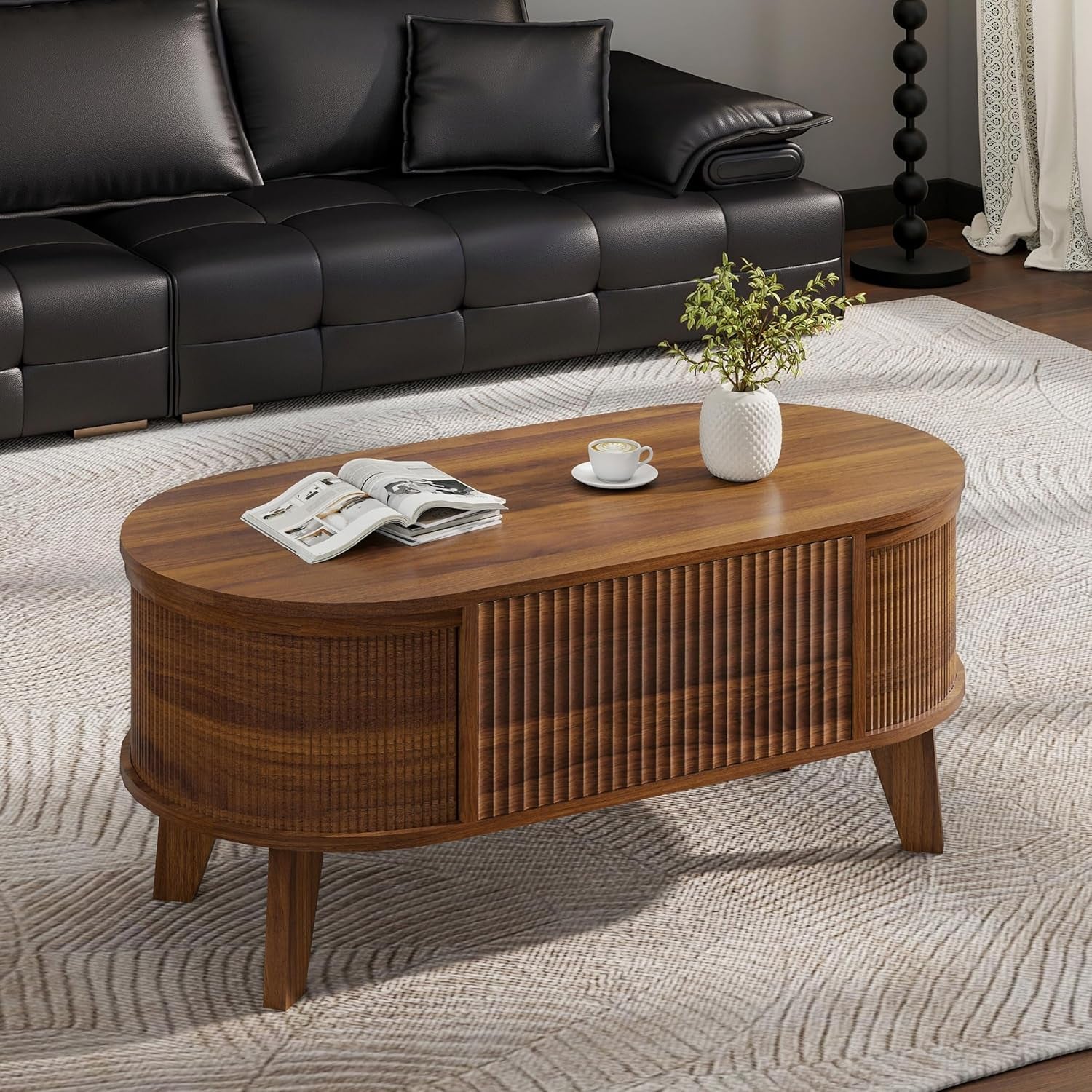 Styled room shot of the walnut oval coffee table with fluted sides and angled legs on a rug
