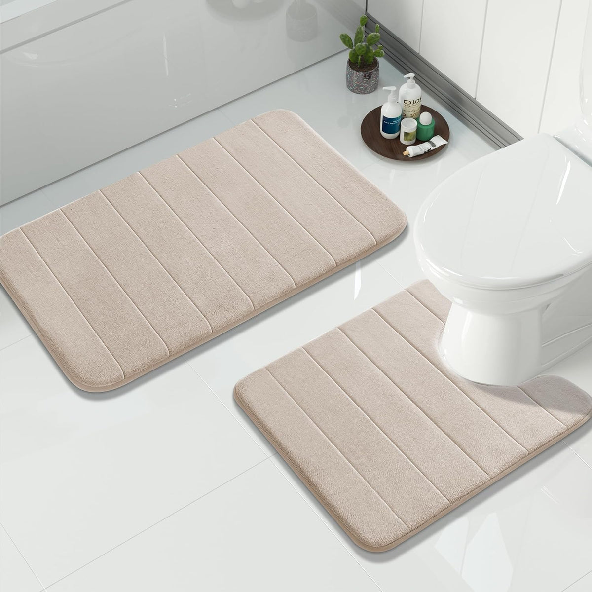 Beige bath mats arranged near a toilet with a small round tray of toiletries and a cactus plant.