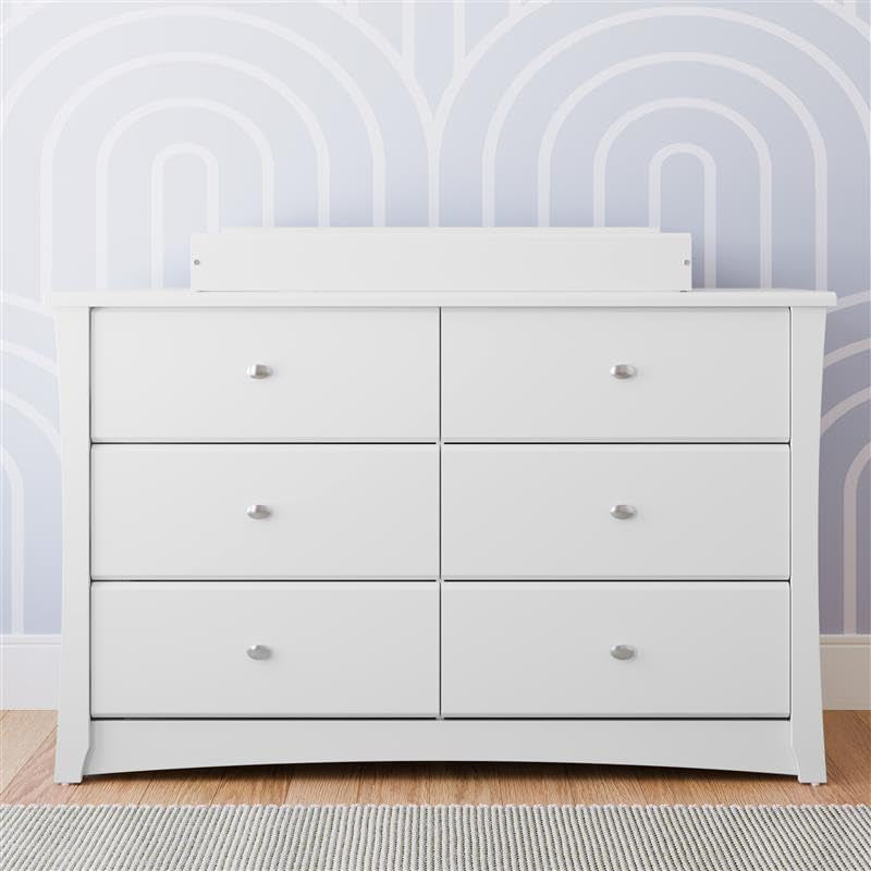 White 6-drawer dresser front view with raised back guard against a patterned wallpapered wall