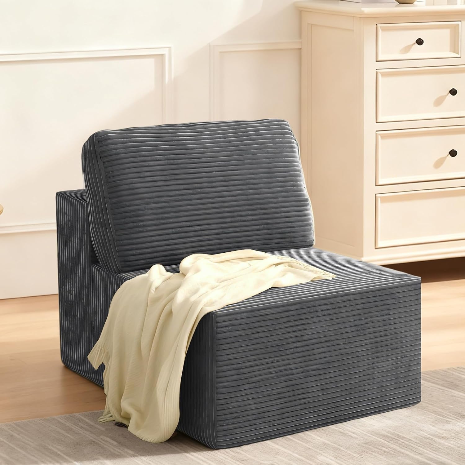Side view of a single armless modular sofa seat in dark gray ribbed fabric with a cream throw draped over it.