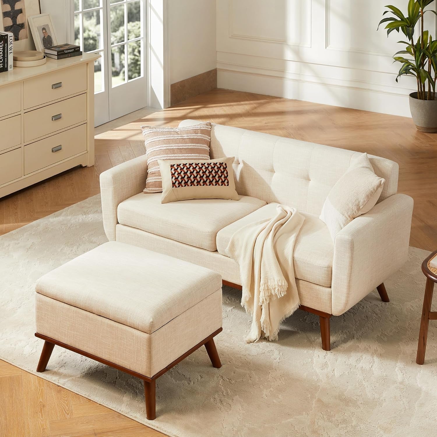 Beige loveseat paired with a matching square ottoman in a sunlit room with wooden floors.