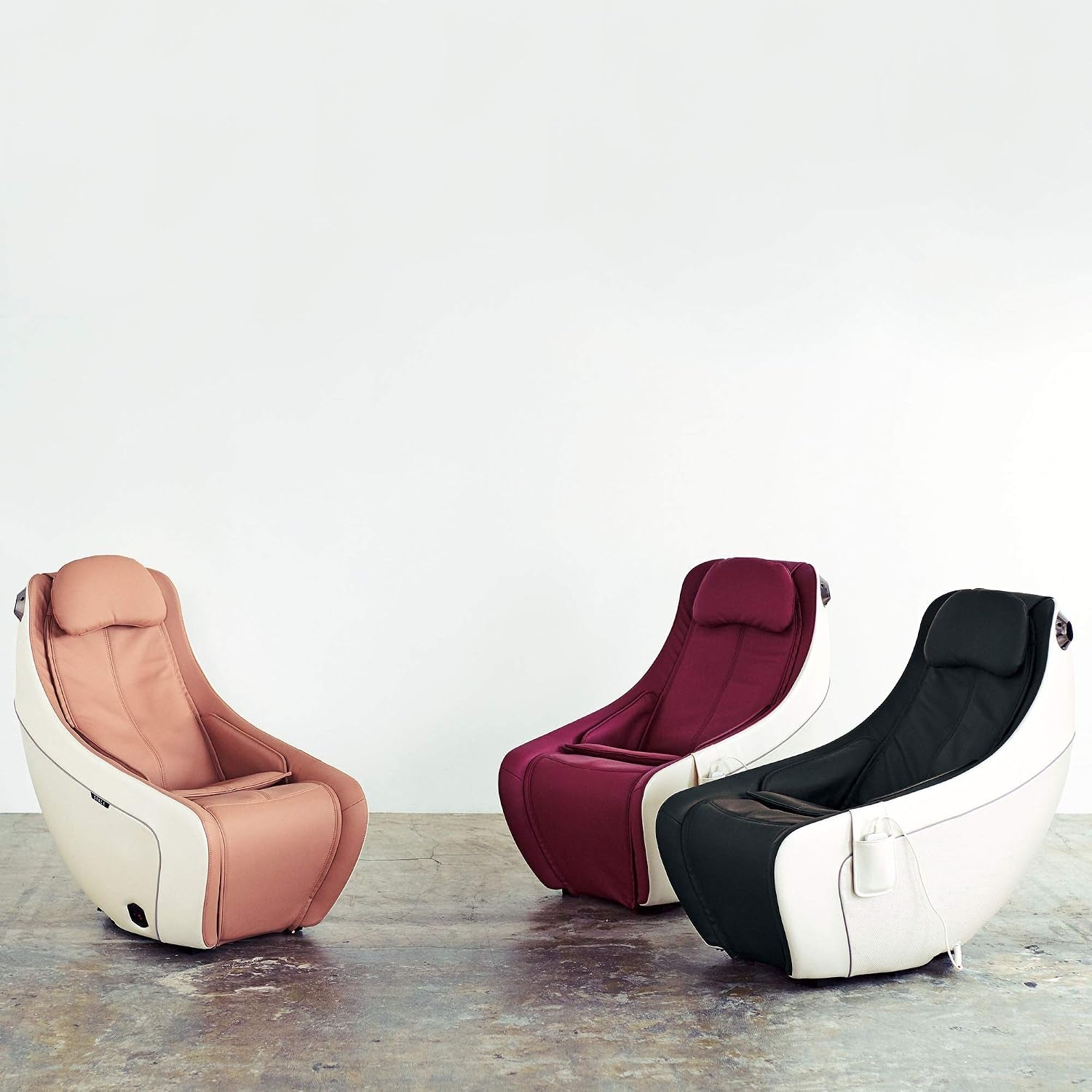 Three massage chairs in beige, wine and black finishes arranged side by side on a concrete floor
