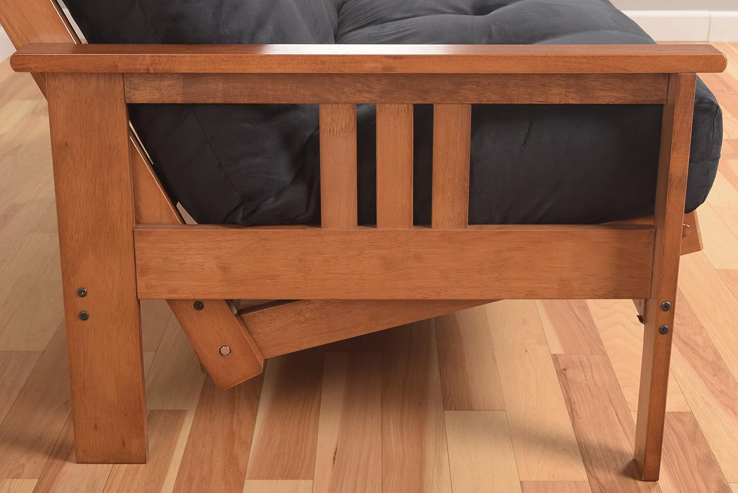 Close side view of wooden arm and leg with a charcoal tufted mattress visible behind the slats