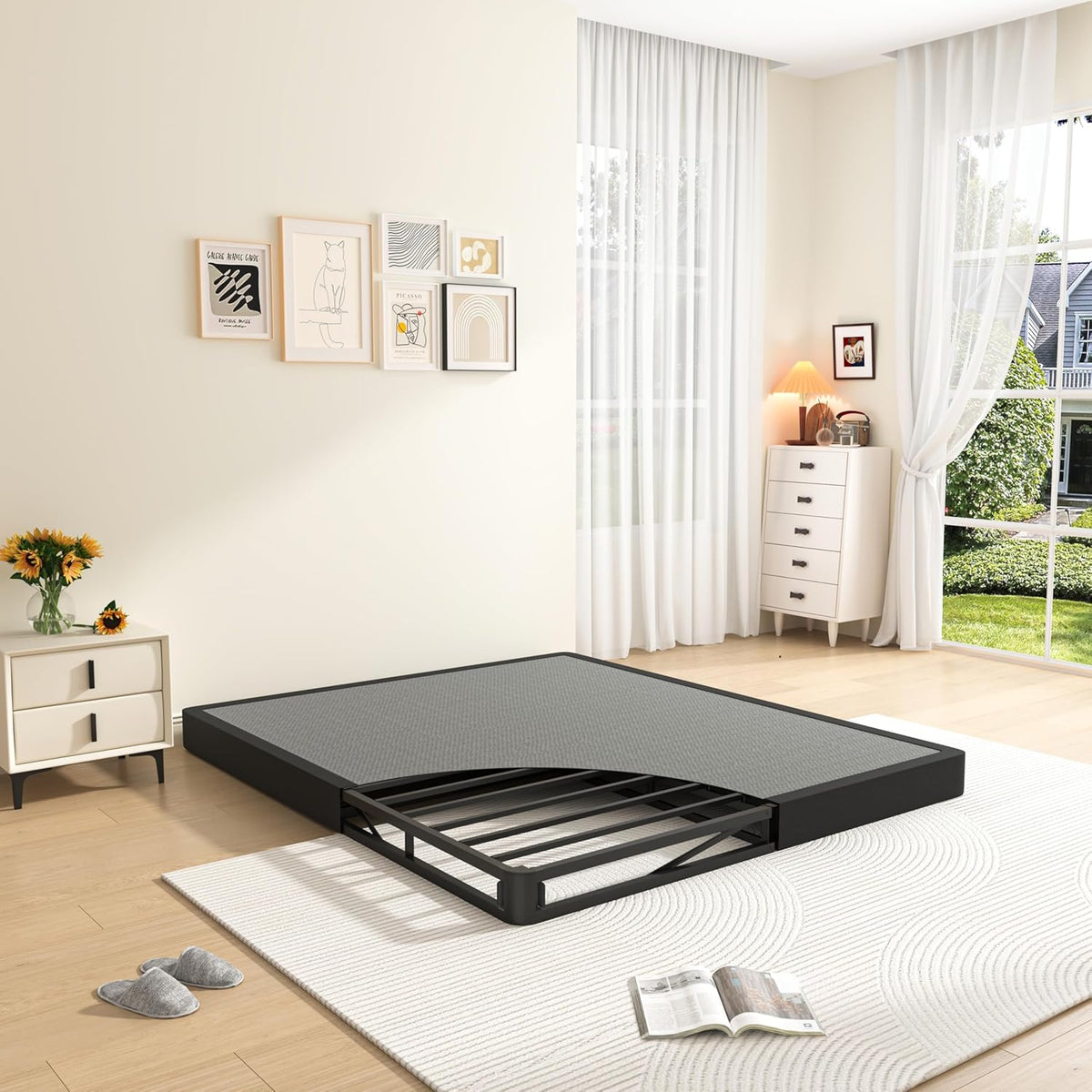 Low black metal bed base with gray top layer and exposed slatted inner frame in a bright bedroom setting