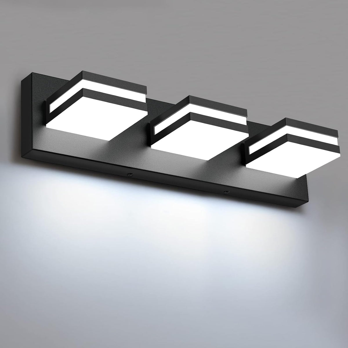 Close-up of a black three-light LED vanity bar on a rectangular backplate, illuminated against a grey wall.