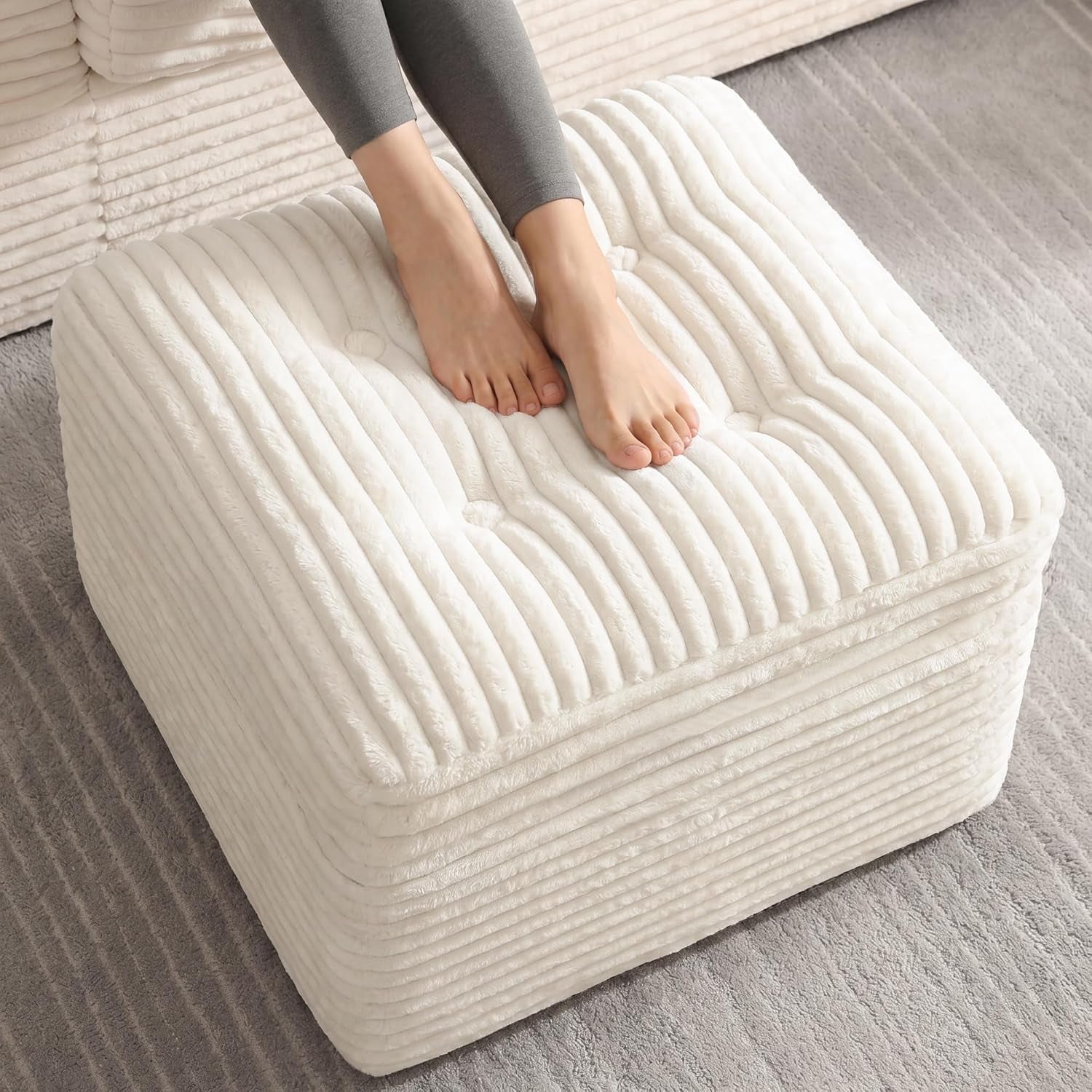 Beige wide-wale corduroy square pouf with feet resting on top, angled top-front view on a rug