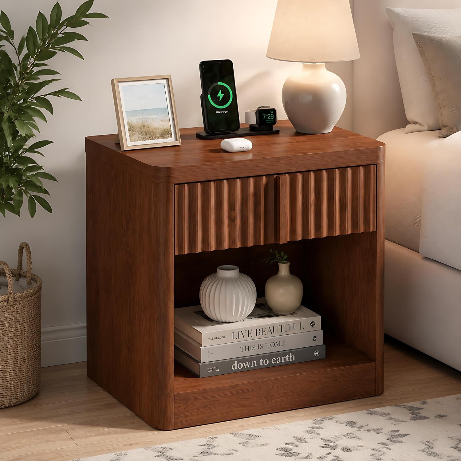 Brown fluted nightstand with open cubby holding vases and stacked books, lamp and charger on top.