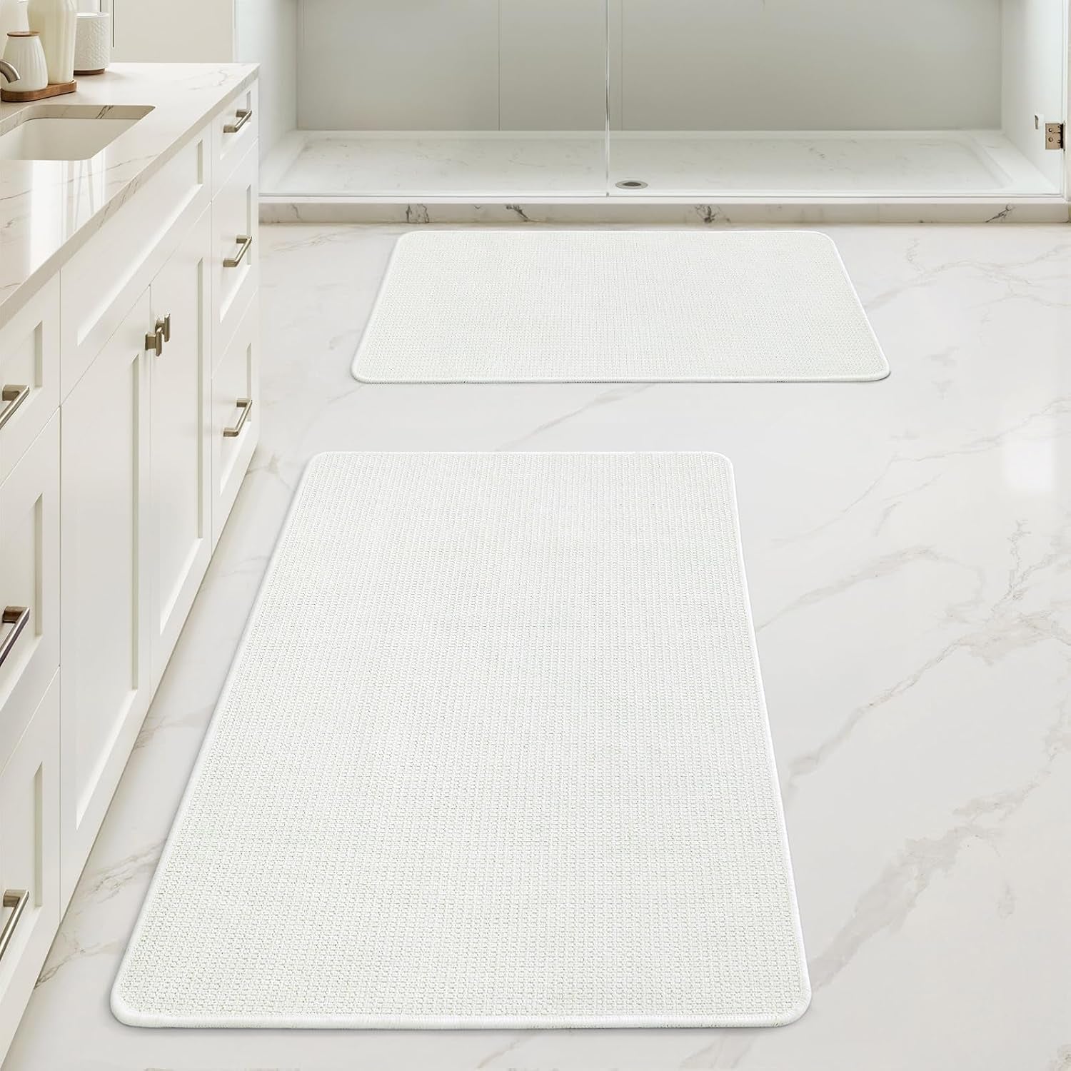 White rectangular bath rugs shown in a bright bathroom in front of a shower and vanity