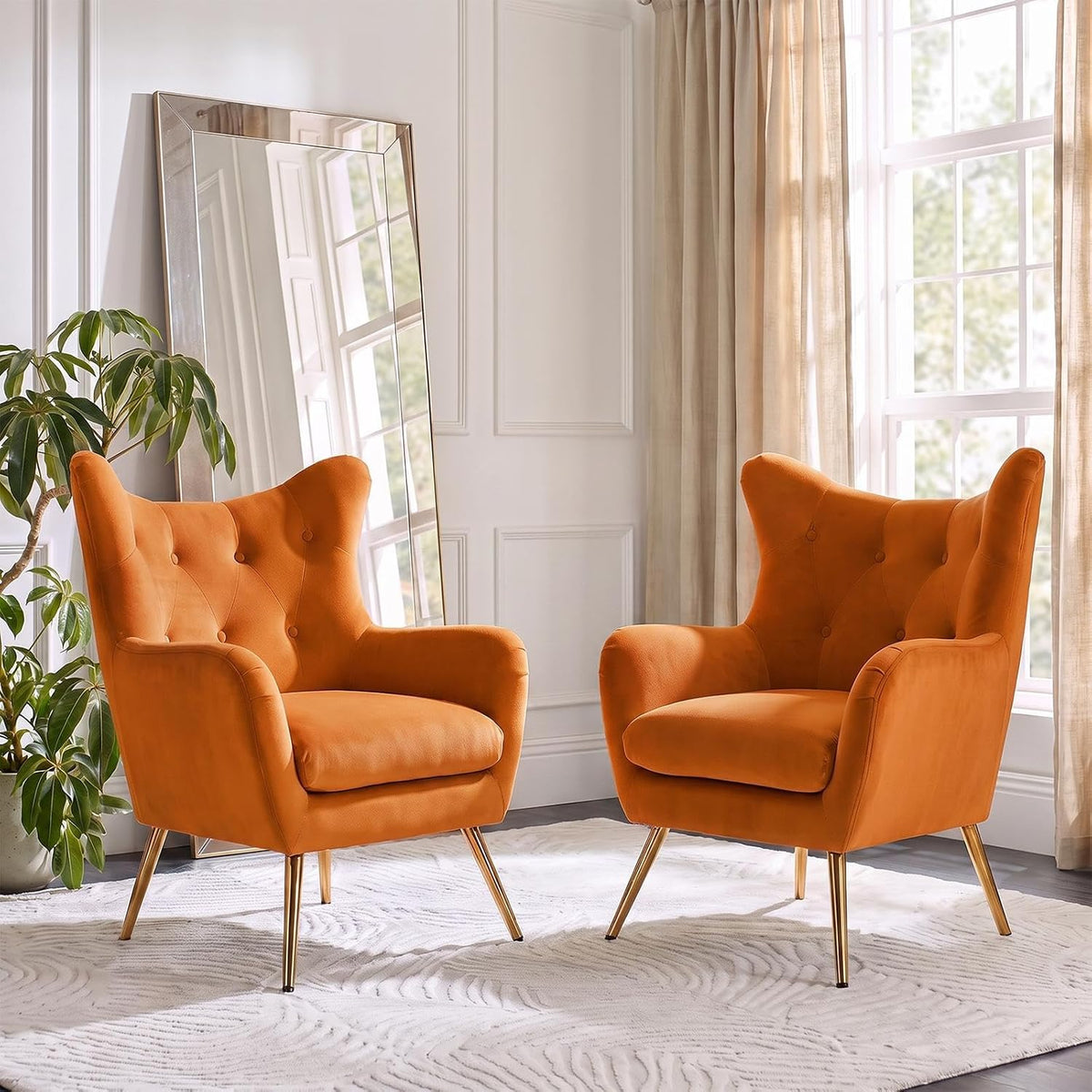 Two burnt-orange velvet wingback chairs arranged near a leaning mirror and window.