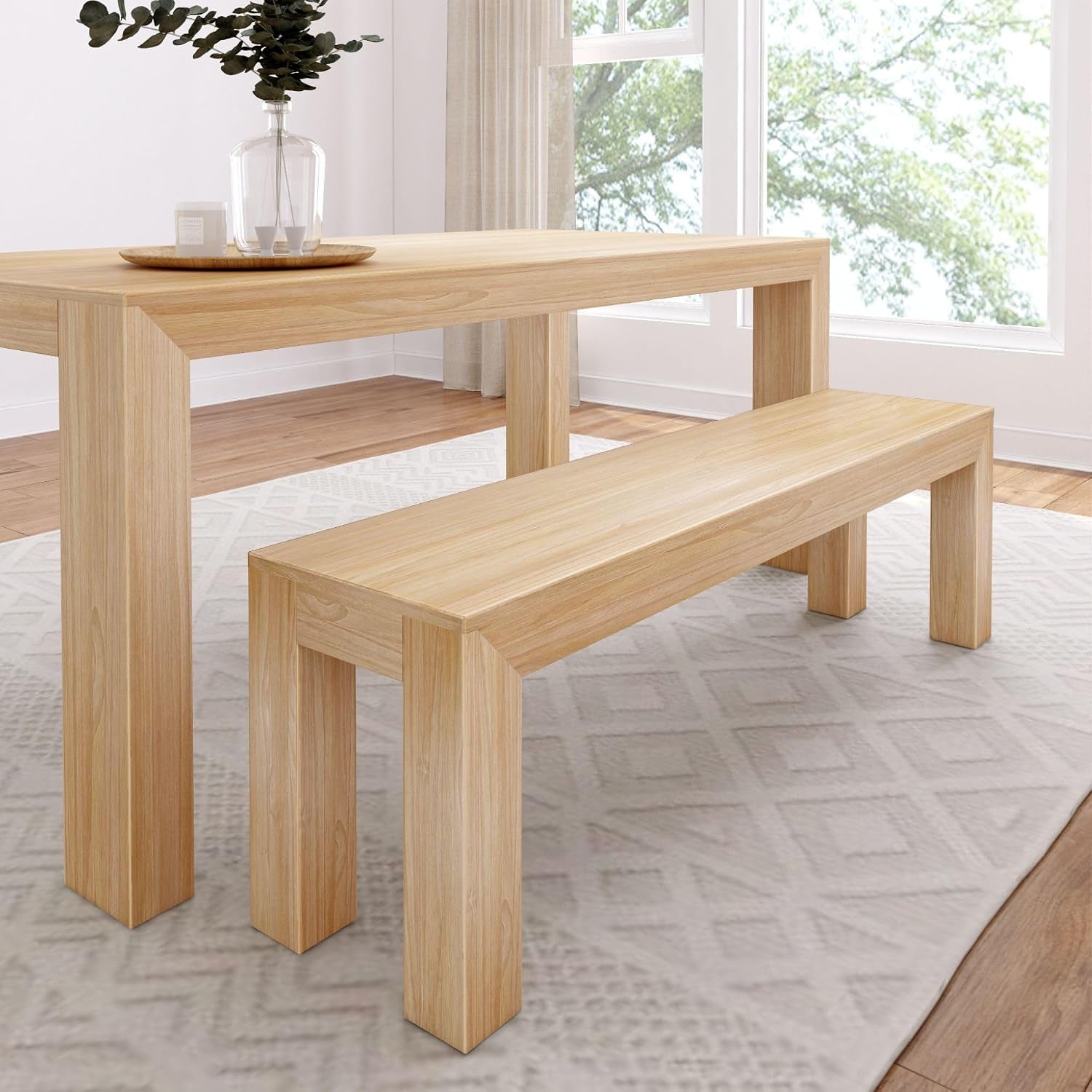 Close side view of a natural wood dining table paired with a matching bench on a rug near windows