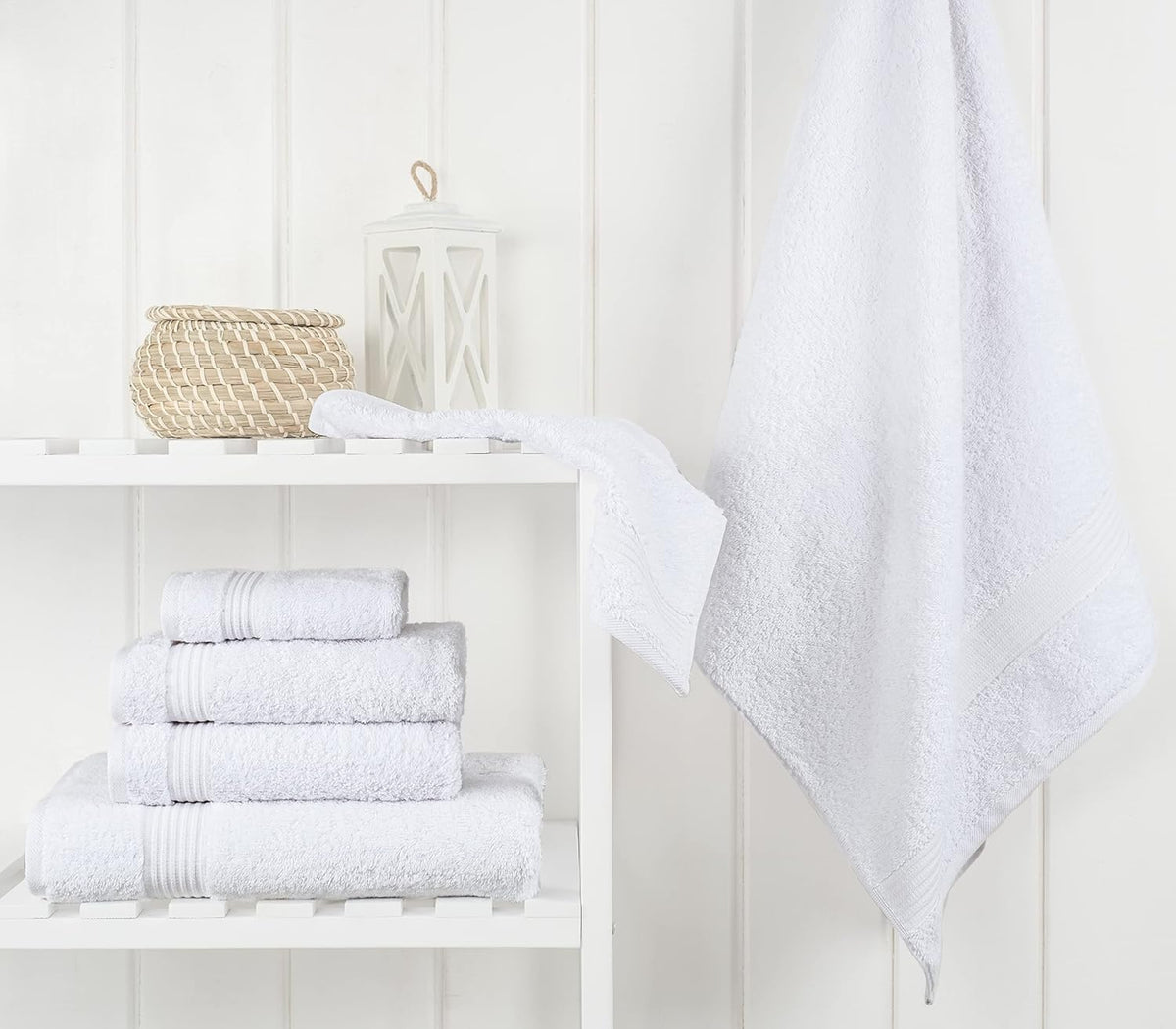 Bathroom shelf with folded white towels, small basket and lantern, and a towel hanging nearby
