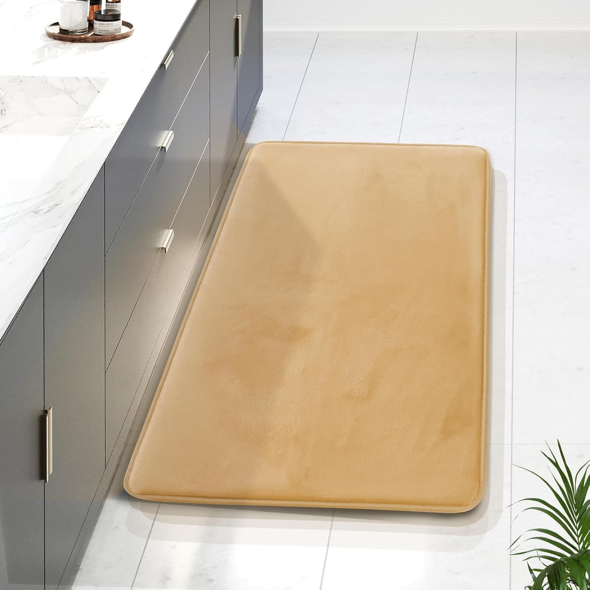 Tan rectangular memory-foam runner beside a gray vanity on white tile, photographed from a high angle
