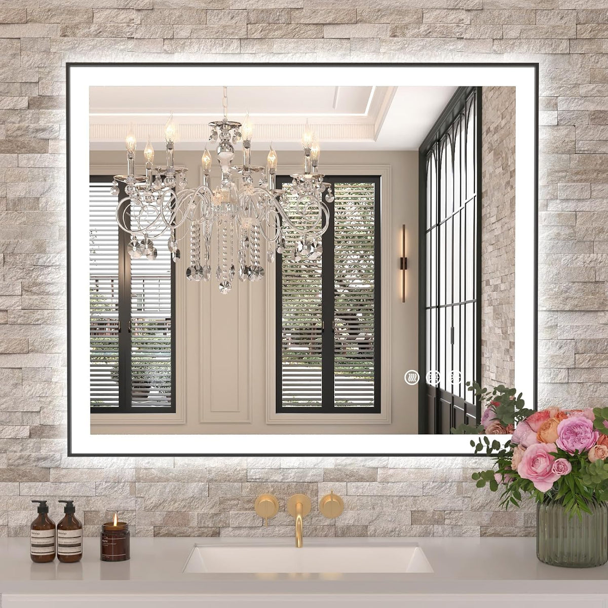 Wall-mounted LED mirror framed by stone tile, reflecting a chandelier and window, vase of flowers on counter.