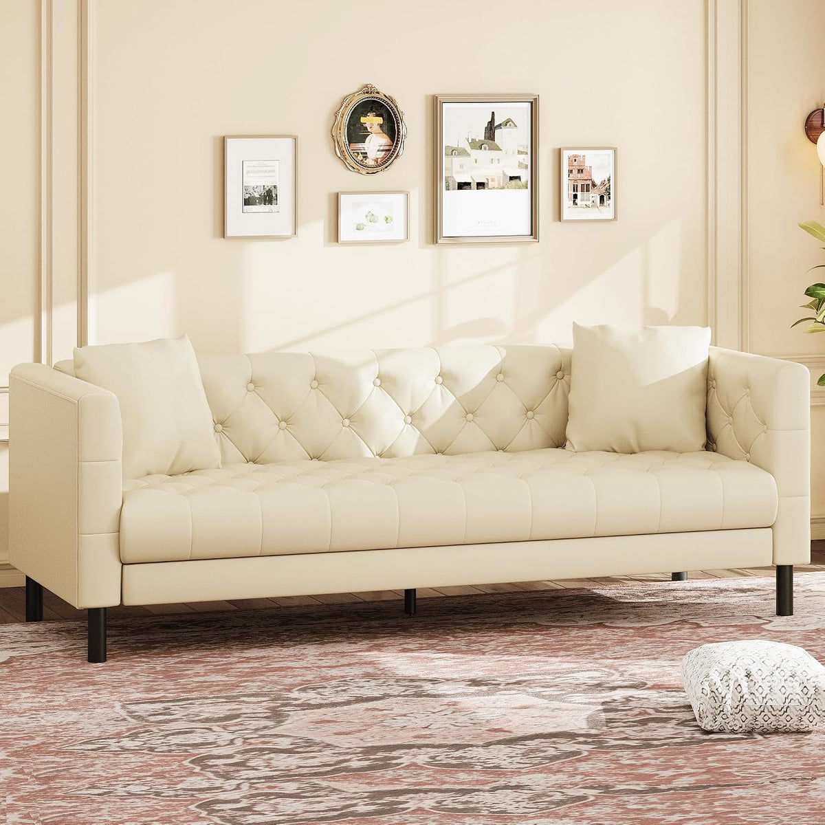 Front view of an ivory tufted three-seat sofa with two pillows in a bright, cream-colored room.