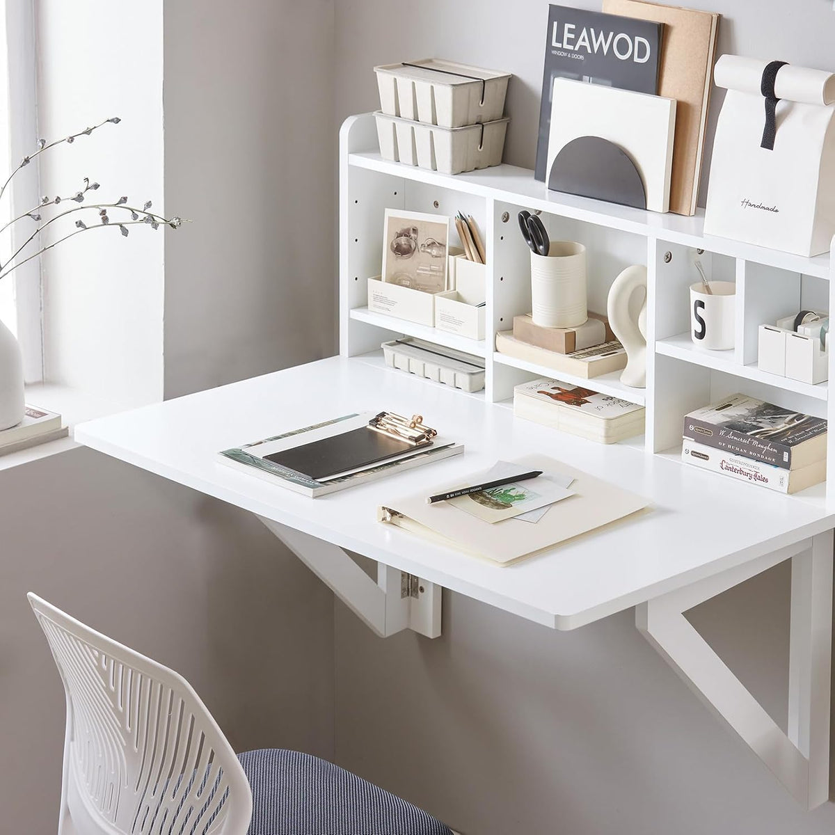White wall-mounted fold-down desk set up with open cubby shelf and chair in a neutral room