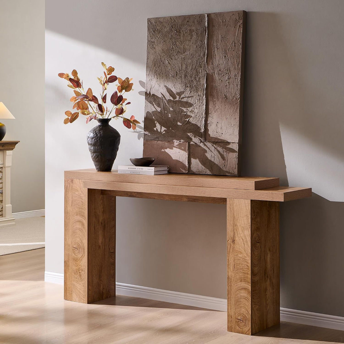 Angled view of the light wood console with a textured panel leaning against the wall and a dark vase on top.